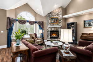 Living area featuring a stone-clad fireplace, high vaulted ceilings, an arched top window, wood-finish flooring, and recessed lighting
