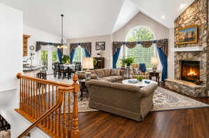 Spacious living area featuring a stone fireplace with hearth, vaulted ceilings, and large arched window
