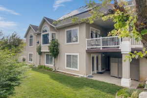 Multi-level stucco exterior featuring a second-story balcony with white railings, a lower-level patio with double French doors, and mature landscaping
