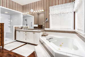 Spacious bathroom featuring a built-in jetted tub, a separate walk-in shower, a double vanity with two sinks, and wood-finish flooring