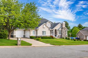 Stucco exterior with stone accents, featuring a multi-car garage, manicured lawn, and mature landscaping