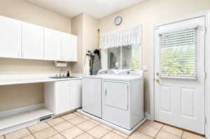 Dedicated laundry space featuring a utility sink, white cabinetry, a window, and tile flooring