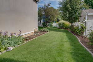 Expansive lawn area featuring a stucco exterior, a white vinyl fence, established perimeter landscaping, and mature trees