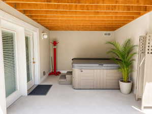 Covered patio with a spa, exposed wood ceiling beams, concrete flooring, and double French doors
