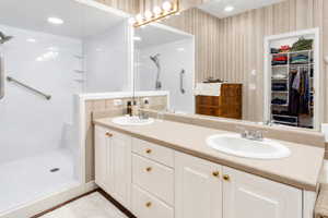 Bathroom featuring a dual vanity with integrated sinks, a full-width mirror, and a walk-in shower with grab bars
