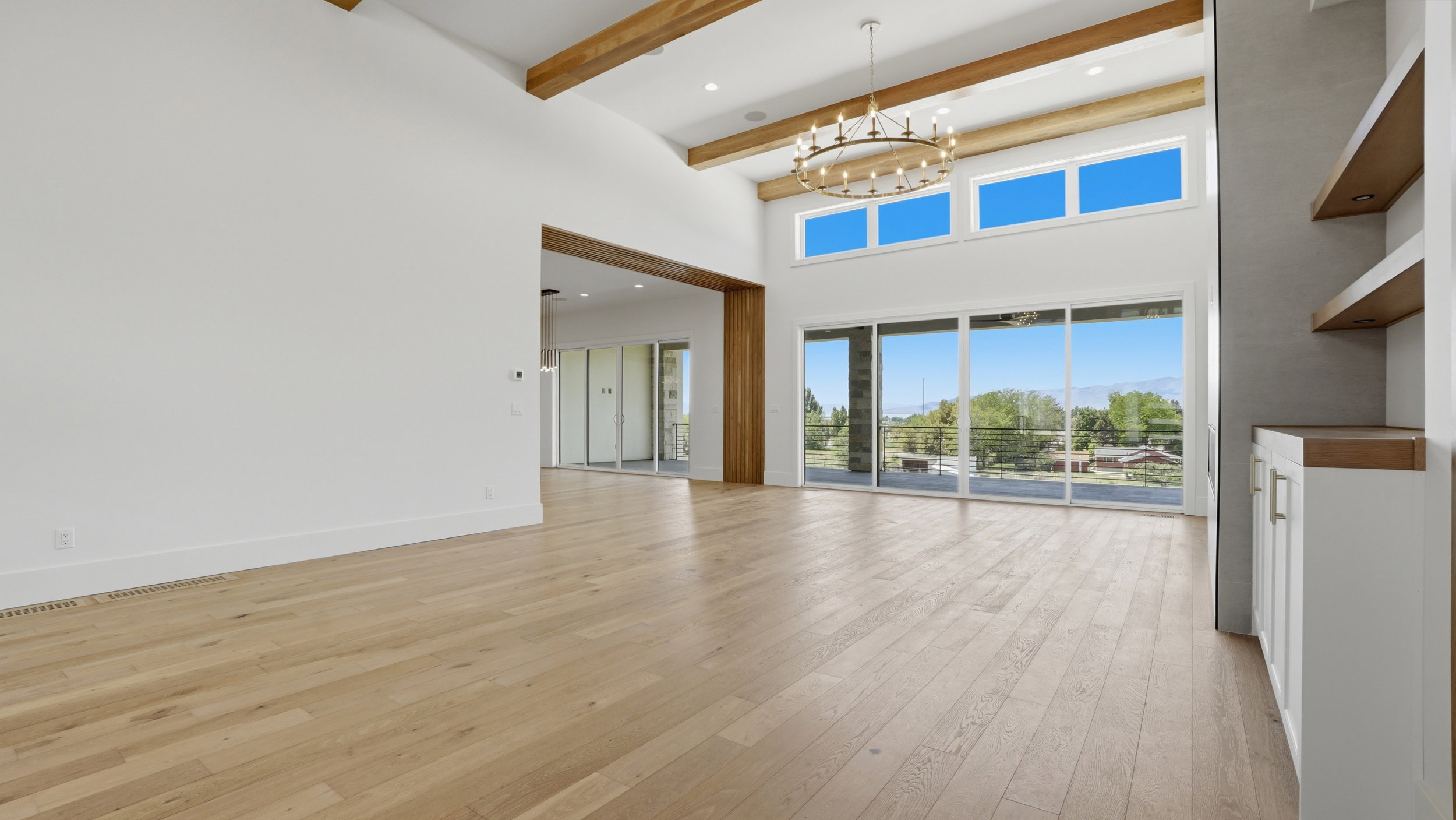 Vaulted ceiling with exposed wood beams, wood-finish flooring, built-in shelving, large sliding glass doors, and a decorative chandelier