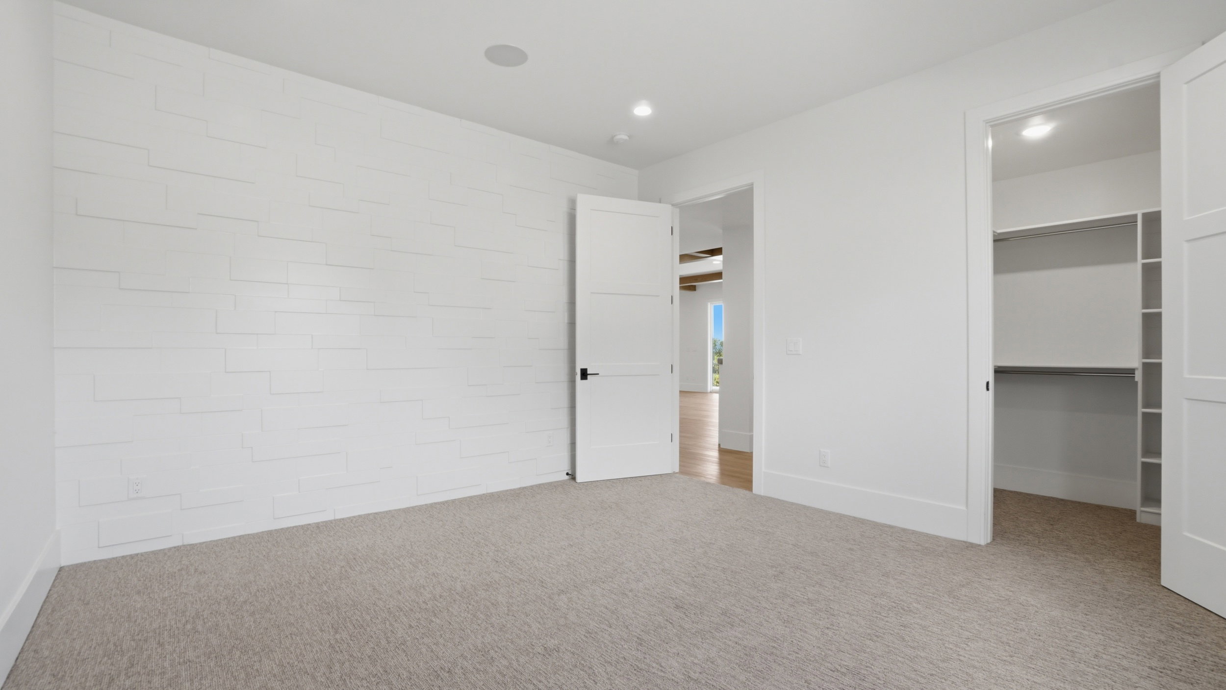 Spacious room featuring light-colored carpeting and a distinctive white accent wall with horizontal paneling