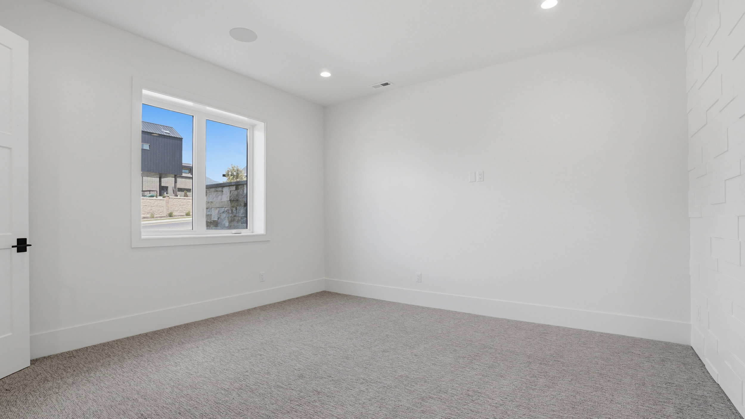 Bright room featuring a multi-pane window, recessed lighting, a built-in ceiling speaker, and a textured accent wall
