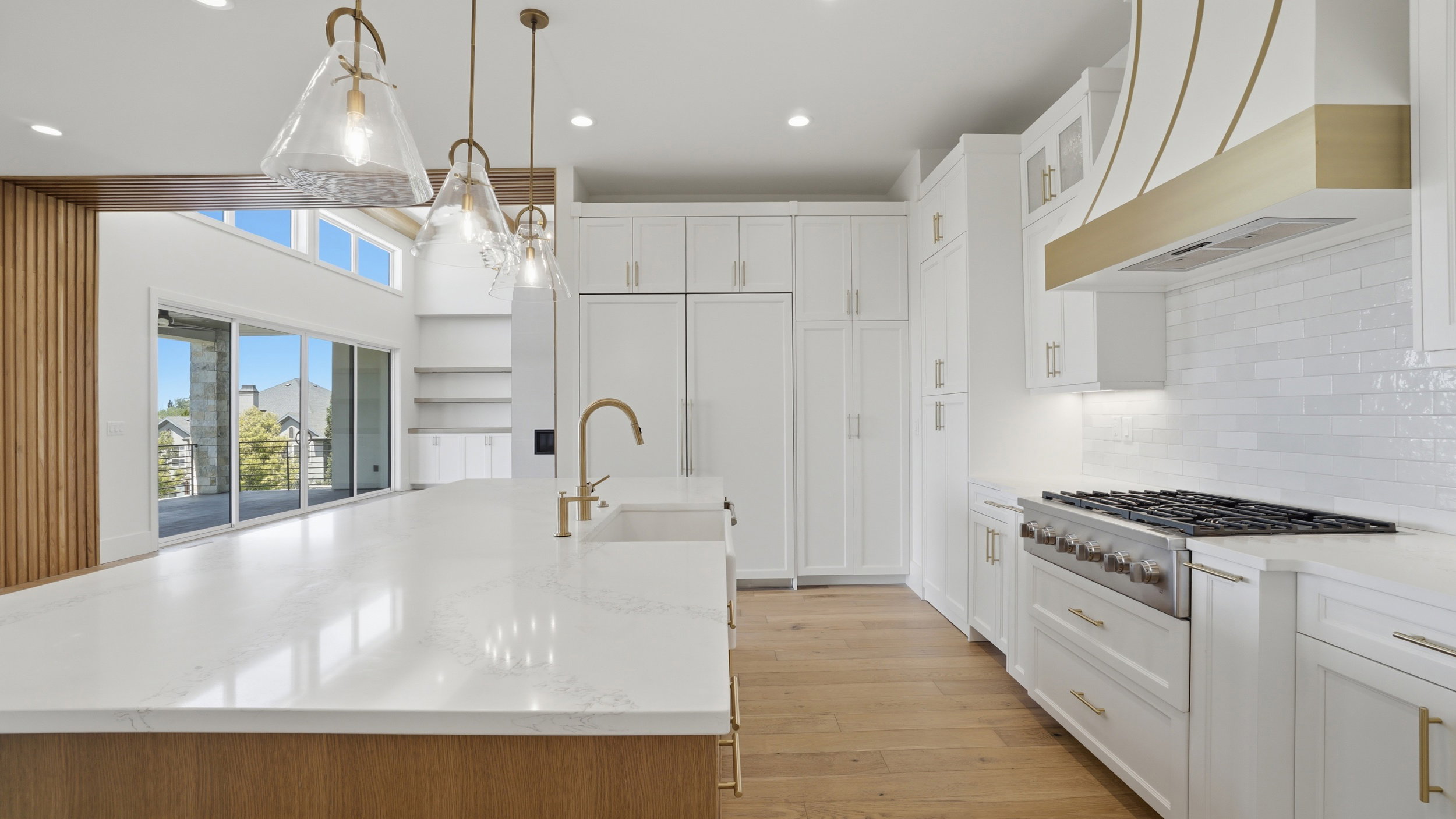 Contemporary kitchen featuring a large island with a light-toned countertop, a professional-grade range, white cabinetry, a decorative range hood, and light wood-finish flooring