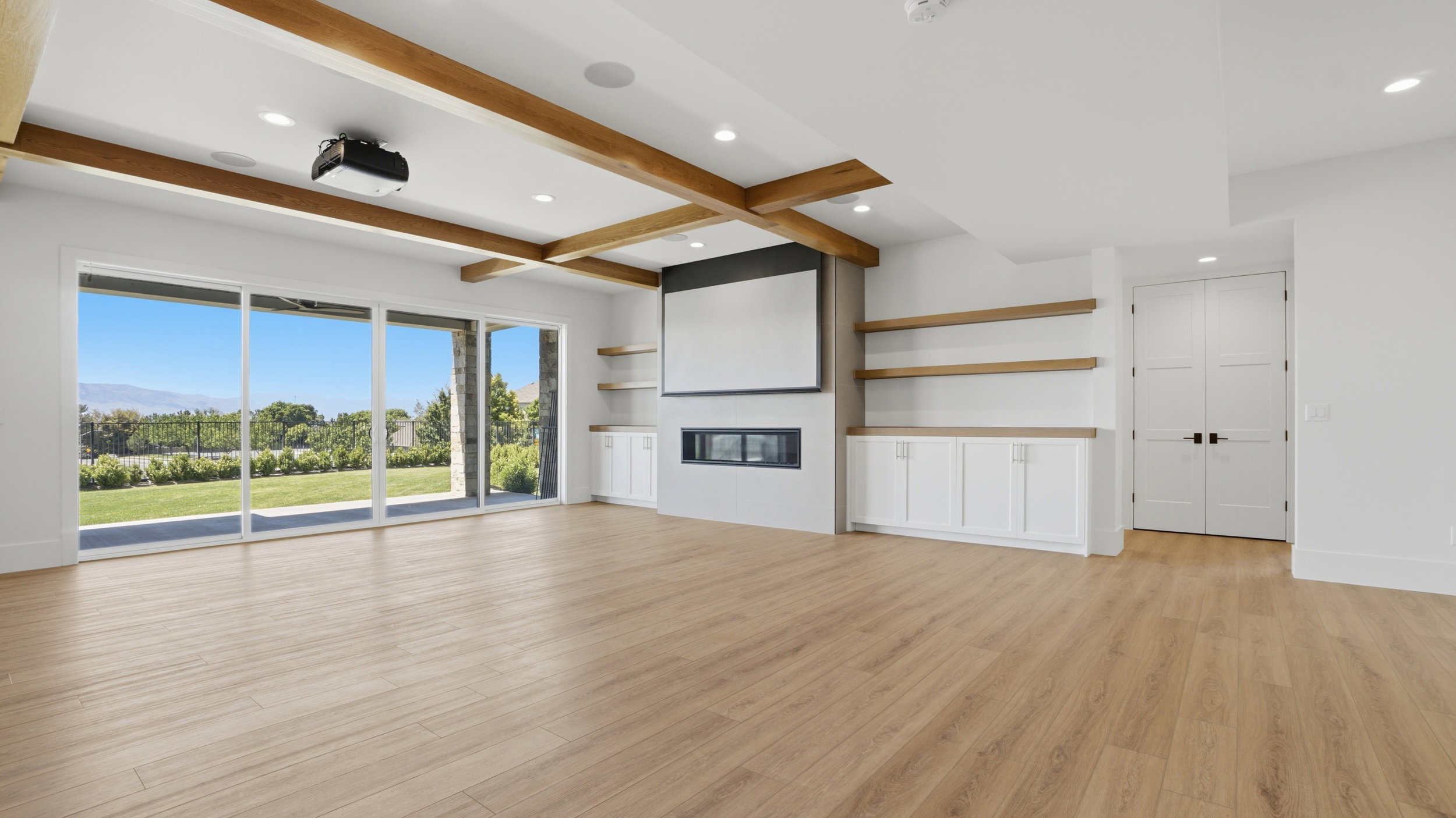 Spacious room featuring wood-finish flooring, exposed ceiling beams, and a built-in media center with a projector screen and fireplace