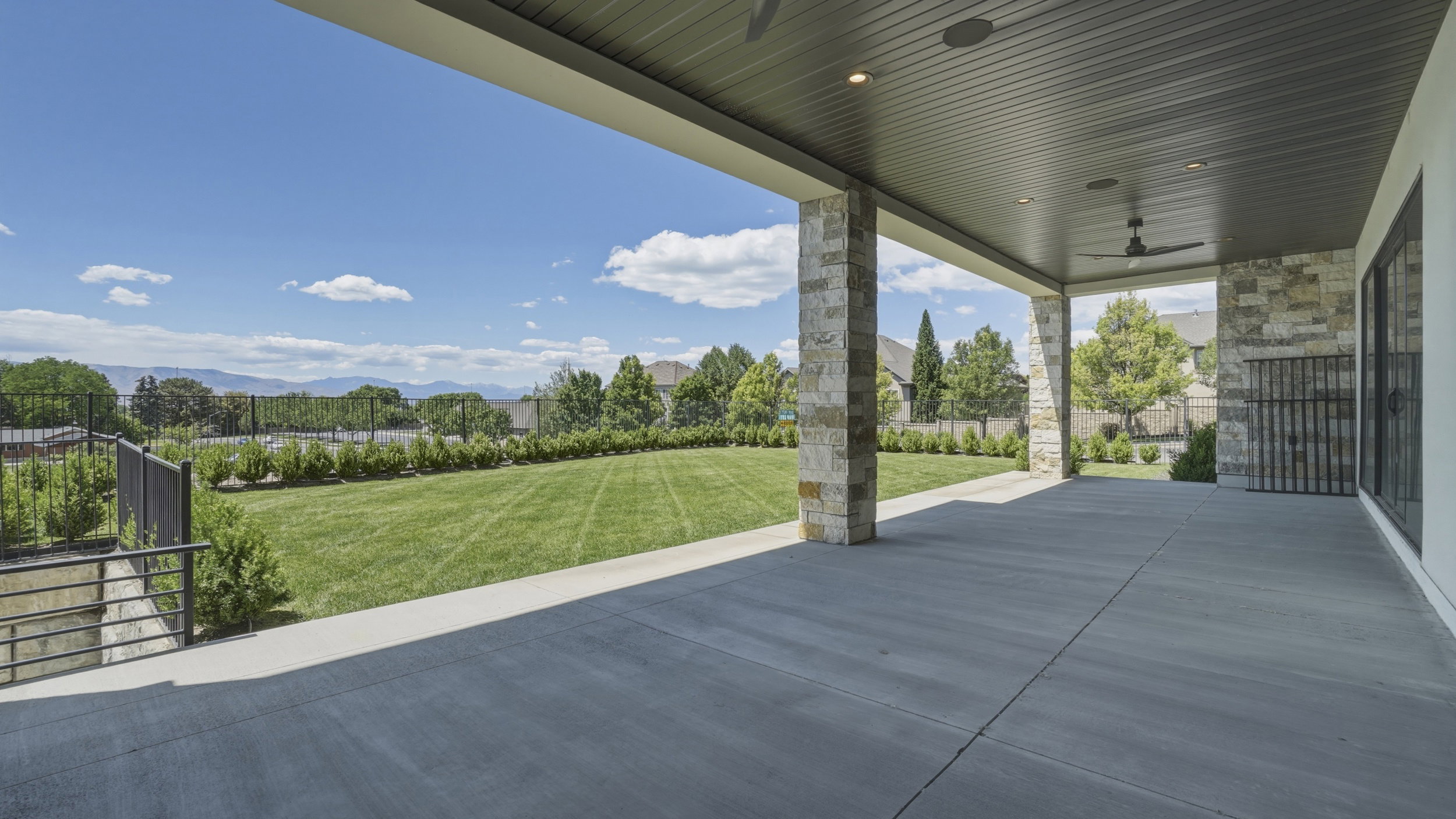 Expansive covered patio featuring stone-clad pillars, recessed lighting, and ceiling fans