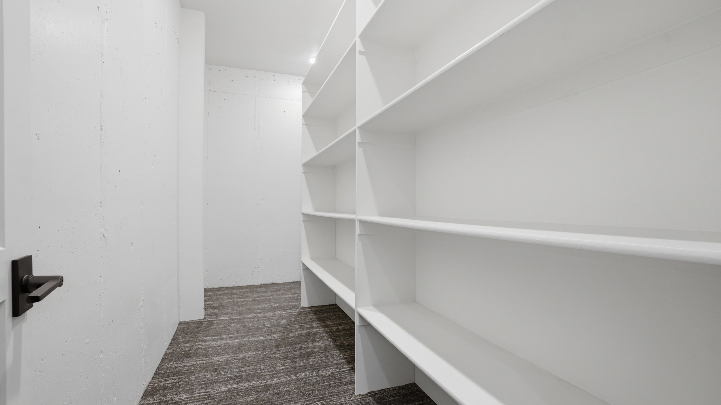Spacious pantry featuring extensive built-in shelving, recessed lighting, and dark wood-finish flooring