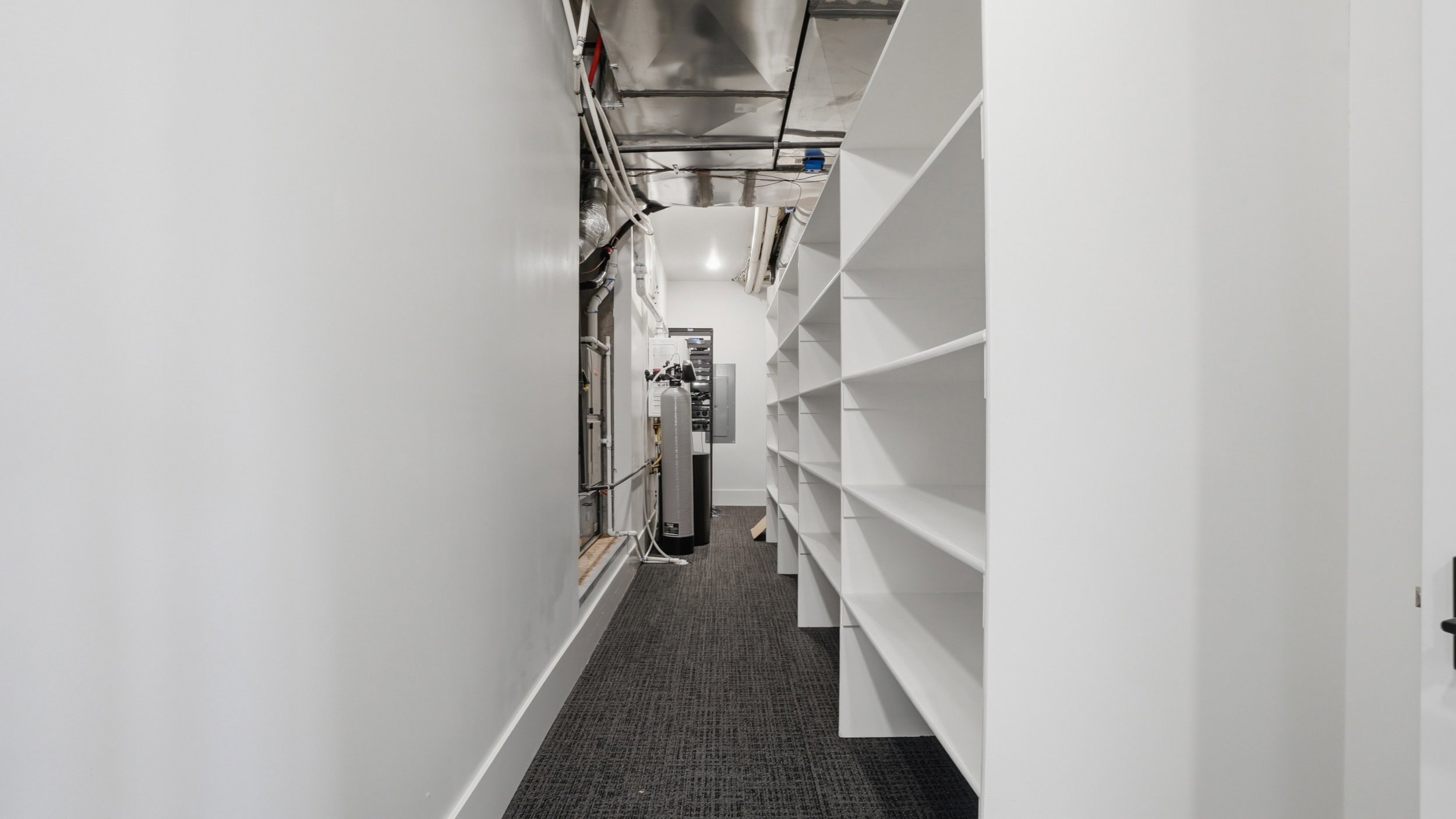 Hallway featuring extensive built-in shelving, white walls, and dark patterned carpeting