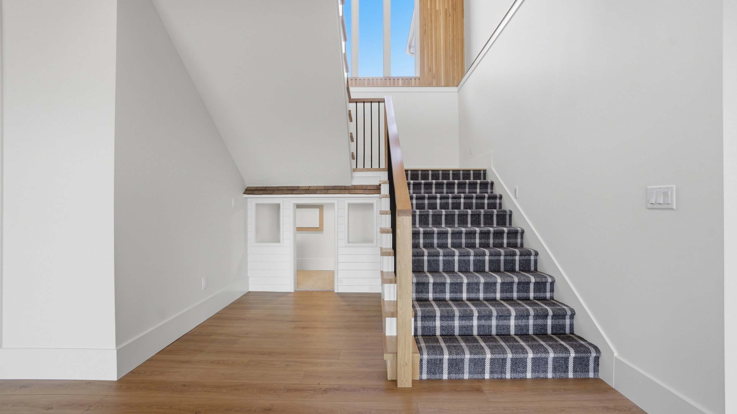Staircase featuring a striped runner, wood-finish flooring, white walls, and a built-in under-stair structure with wood trim and white paneling