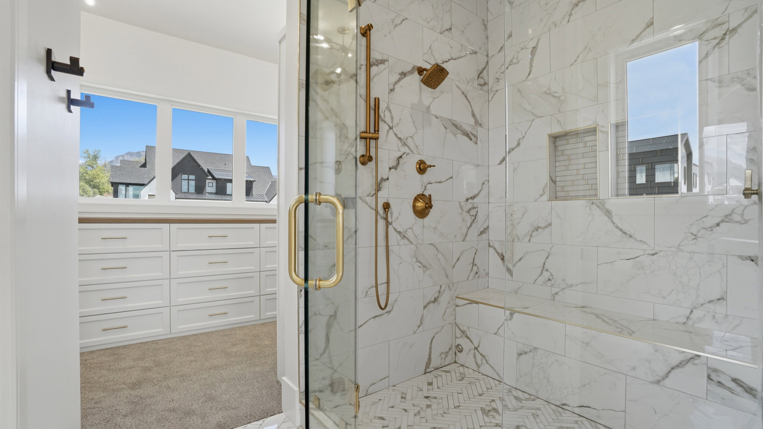 Glass-enclosed shower featuring large format wall tile, a built-in shower bench, and gold-finish fixtures