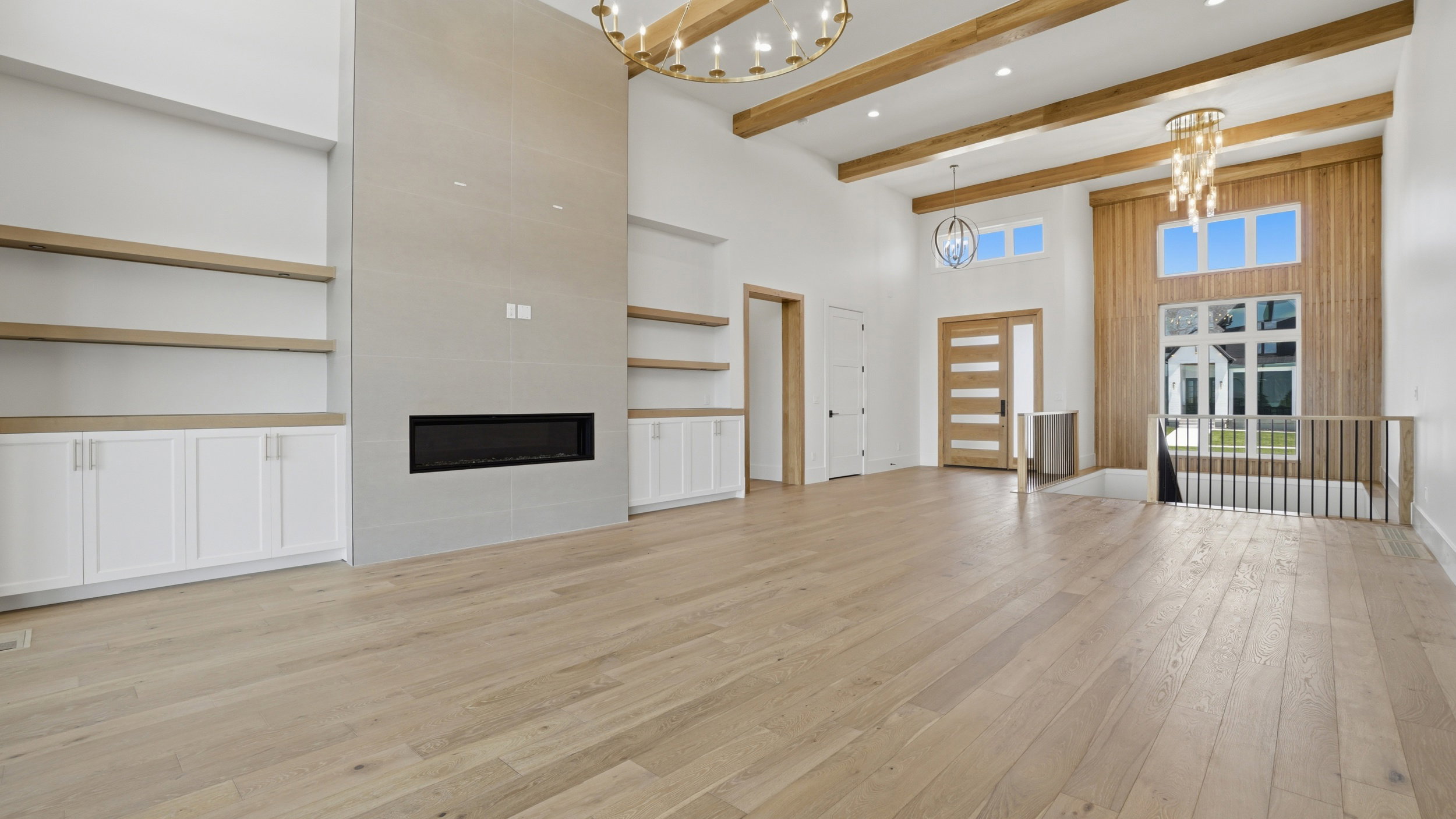 Spacious living area featuring high ceilings with exposed wood beams, a prominent fireplace with a sleek linear insert, light wood-finish flooring, and built-in shelving with lower cabinetry