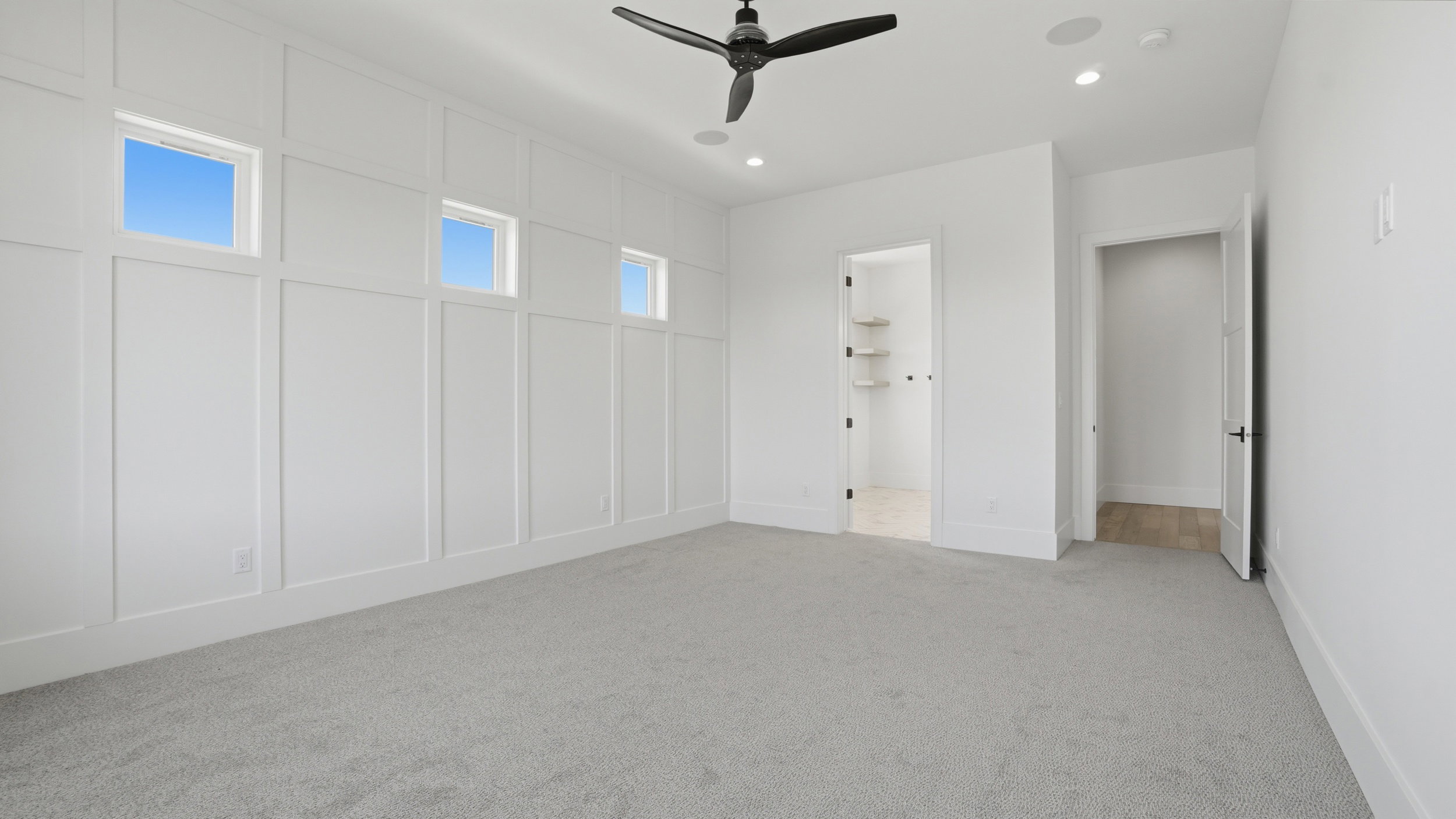 Spacious room with light gray carpeting, crisp white walls featuring board and batten detailing, and high transom windows