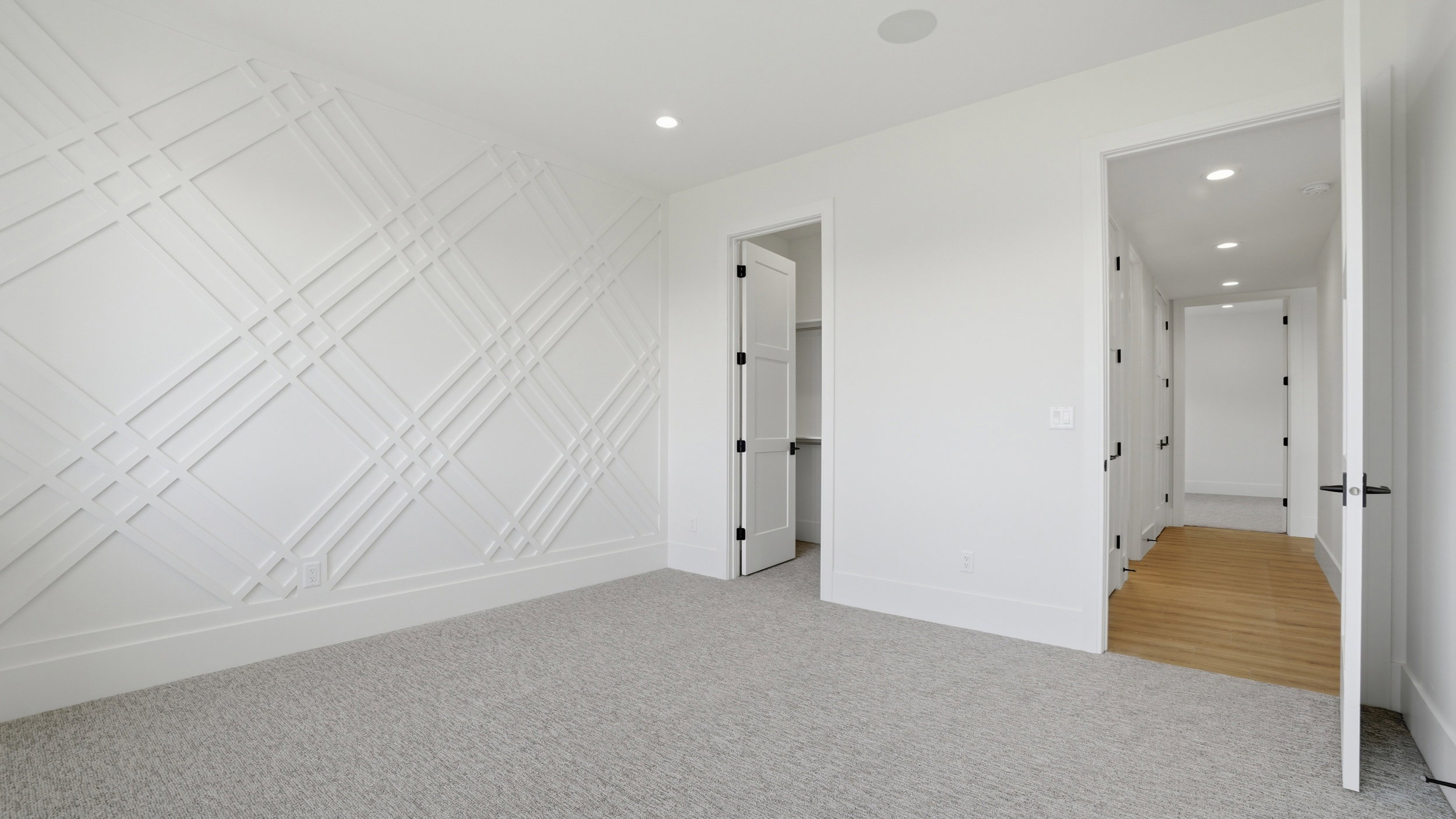 Room featuring a decorative accent wall with geometric paneling, light-colored carpeting, recessed lighting, and a doorway to a closet with bi-fold doors