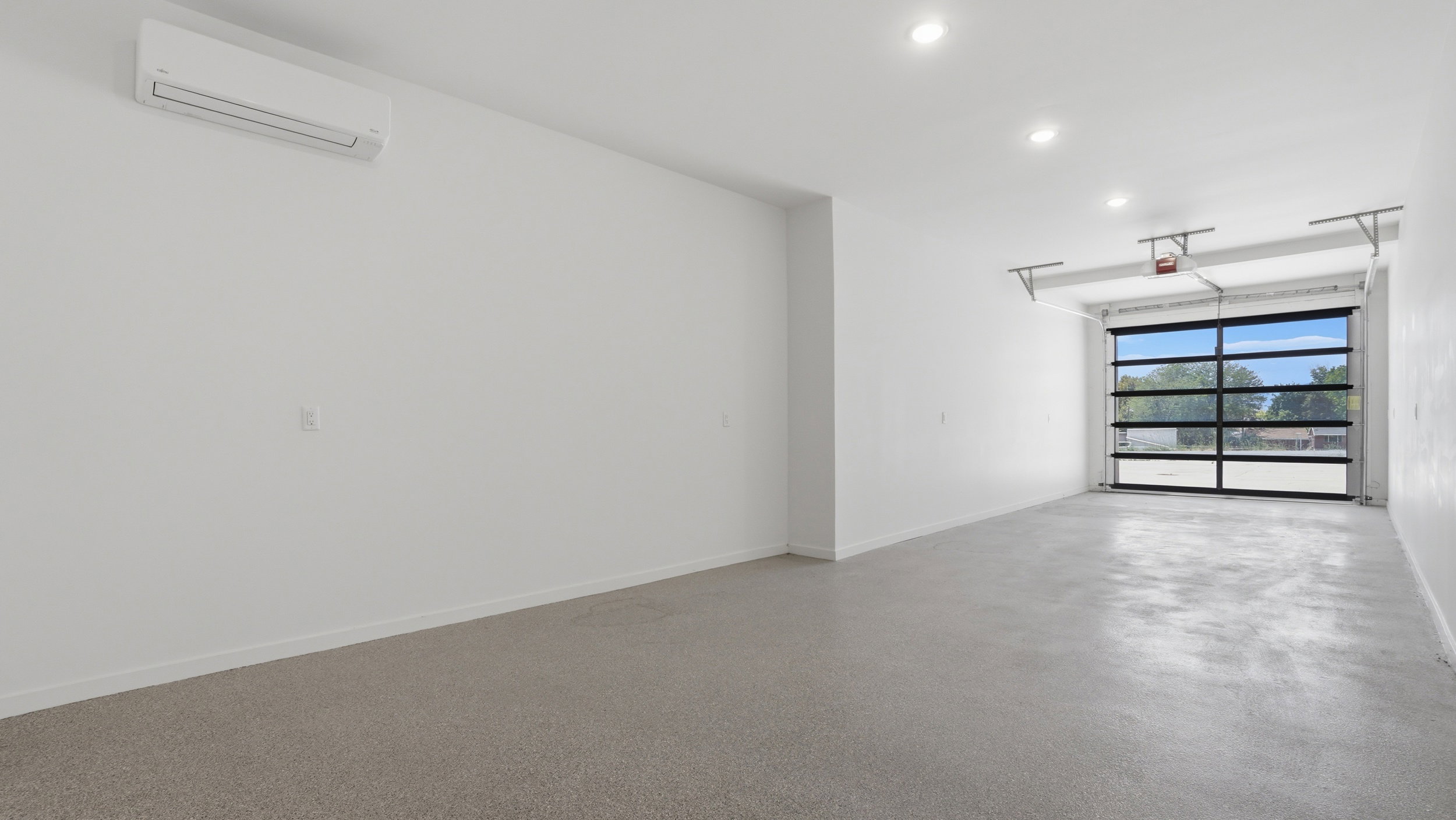 Spacious interior featuring a full-view garage door, recessed lighting, polished concrete flooring, and a wall-mounted mini-split HVAC unit