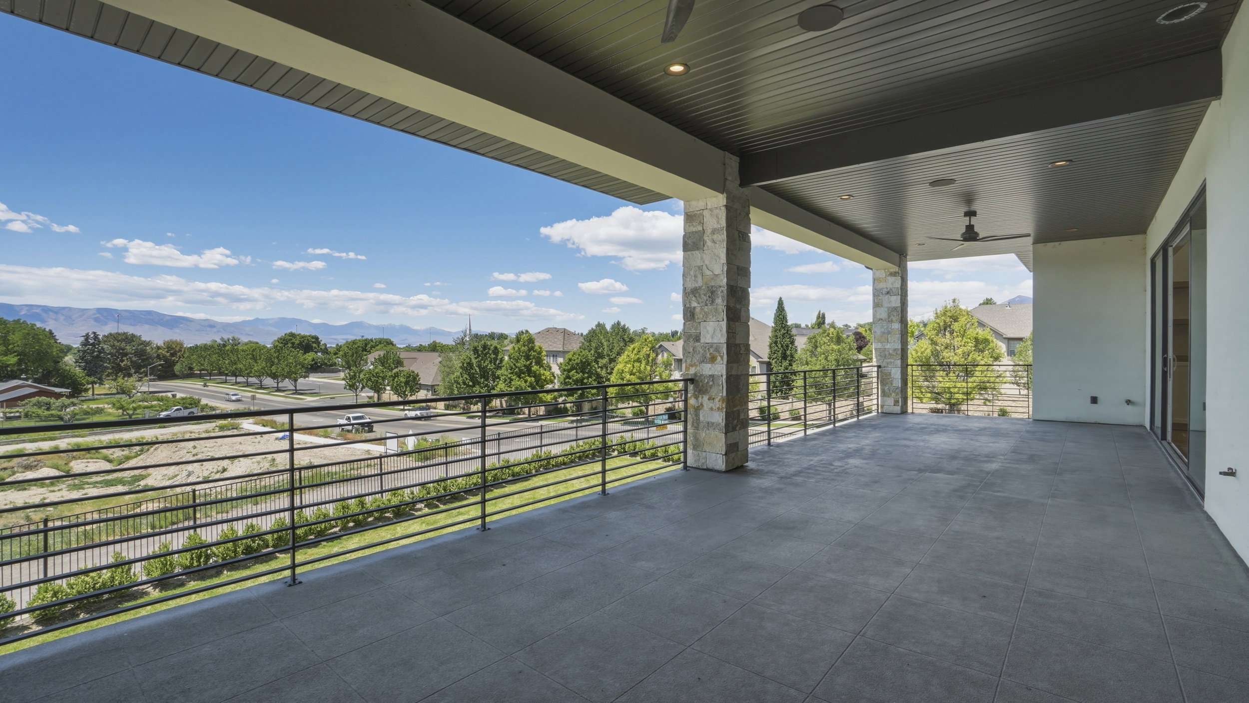 Spacious covered balcony featuring stone-clad pillars, a dark wood-finish ceiling, and a ceiling fan
