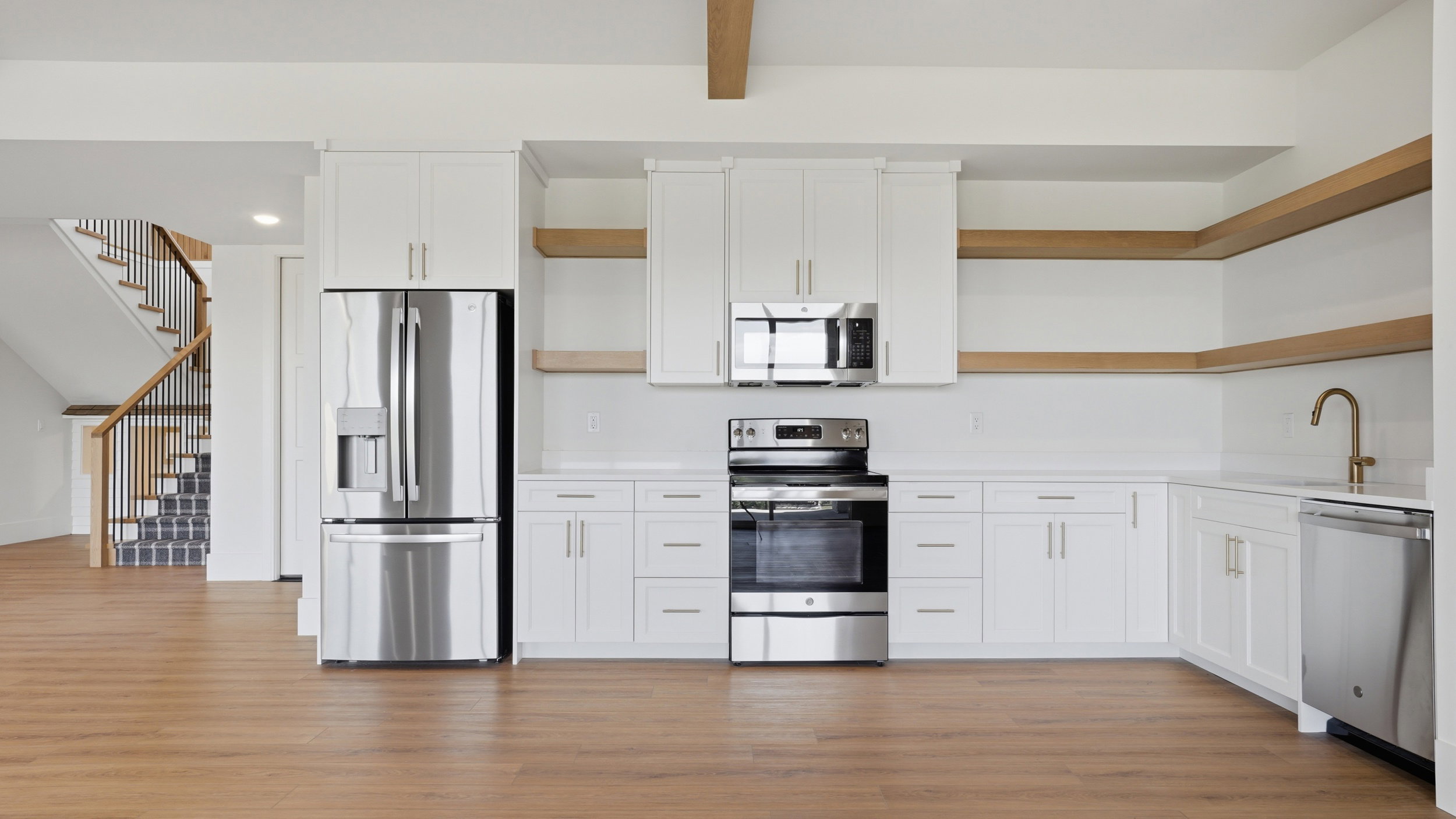 Modern kitchen featuring white shaker cabinetry, stainless steel appliances, open shelving, and wood-finish flooring