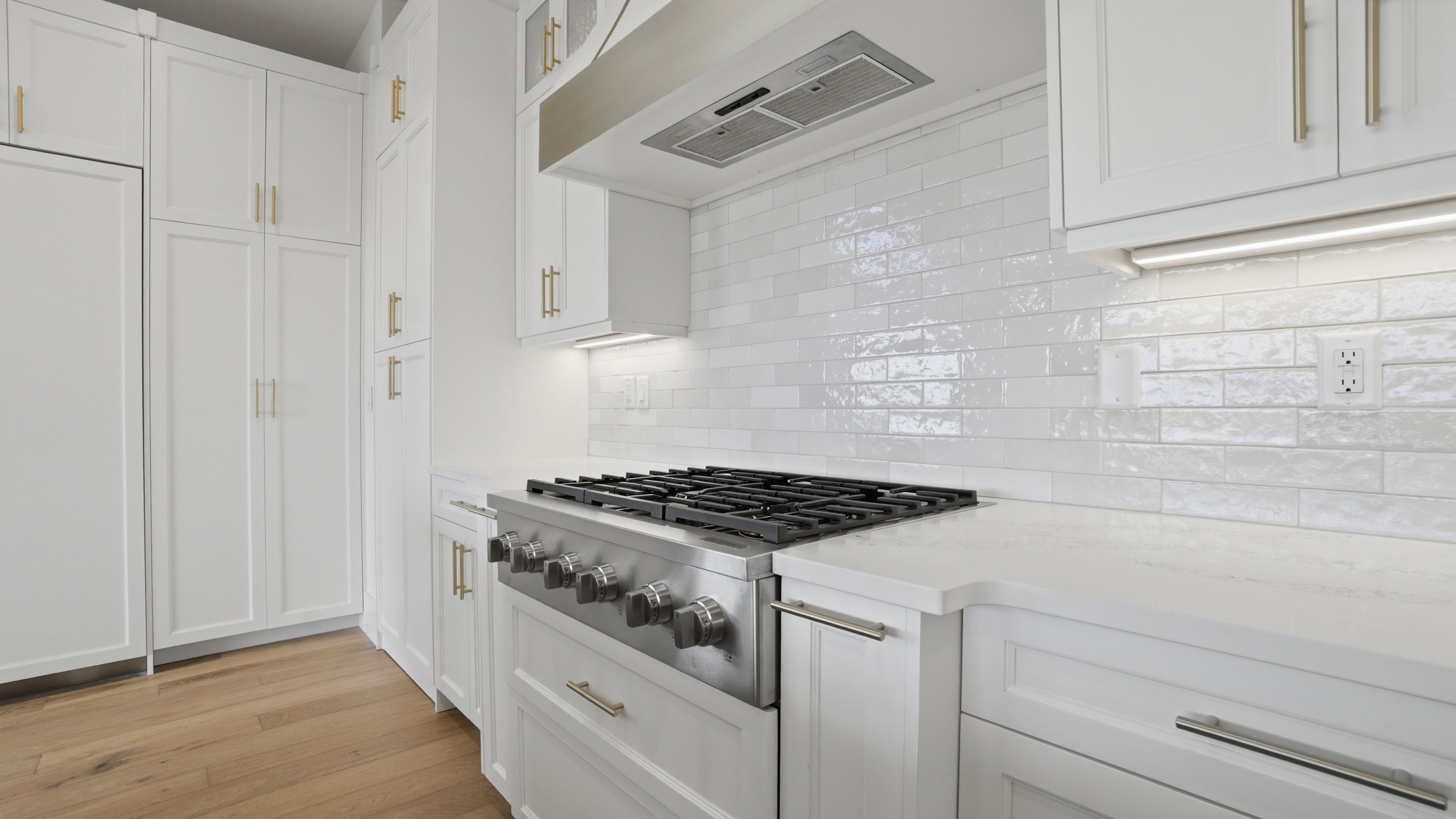 Gourmet kitchen featuring a stainless steel range with a professional-grade hood, white shaker cabinetry with gold-tone hardware, white subway tile backsplash, and light wood-finish flooring