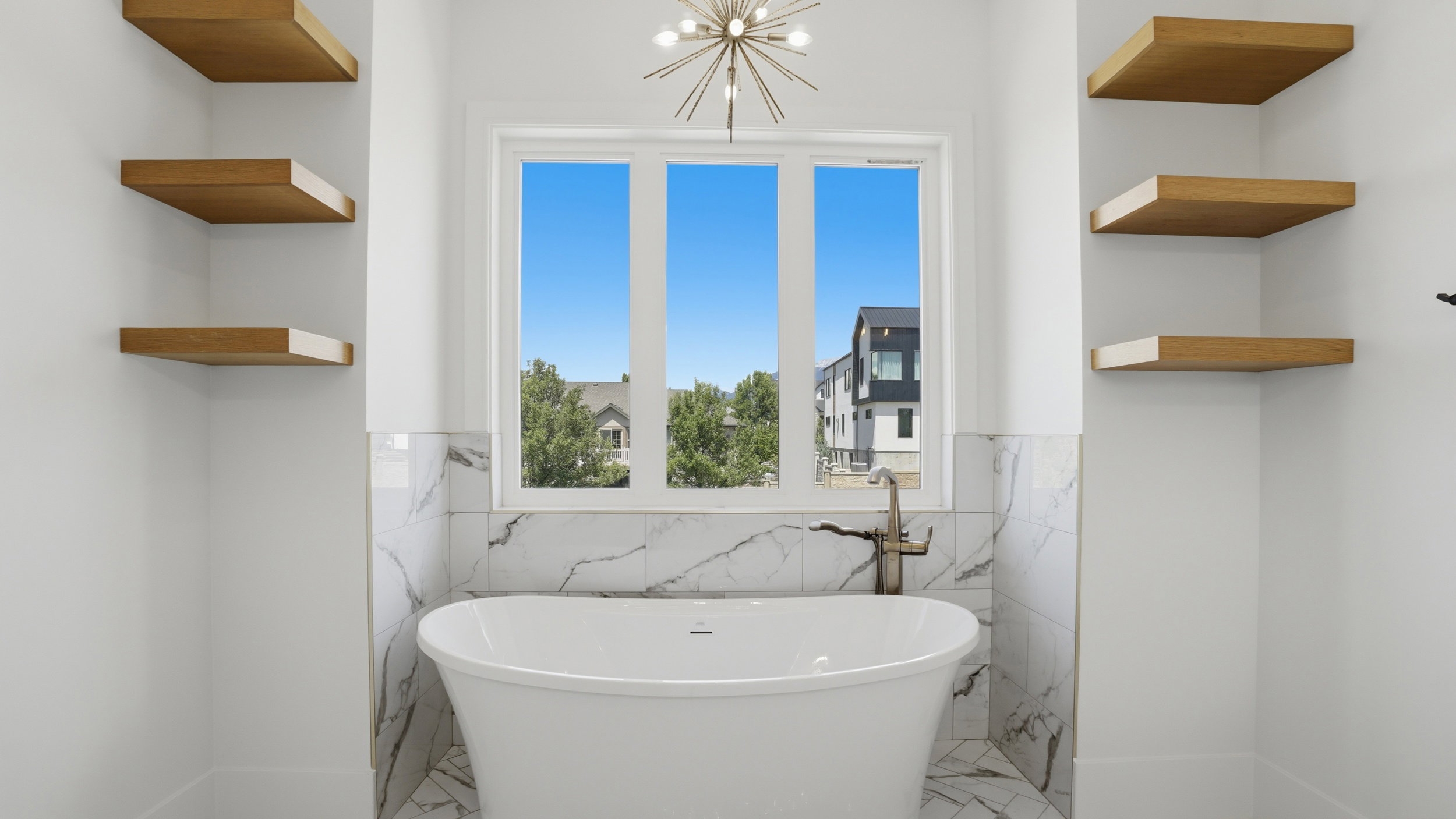 Freestanding soaking tub with floor-mounted faucet, surrounded by marble-style tile wainscoting