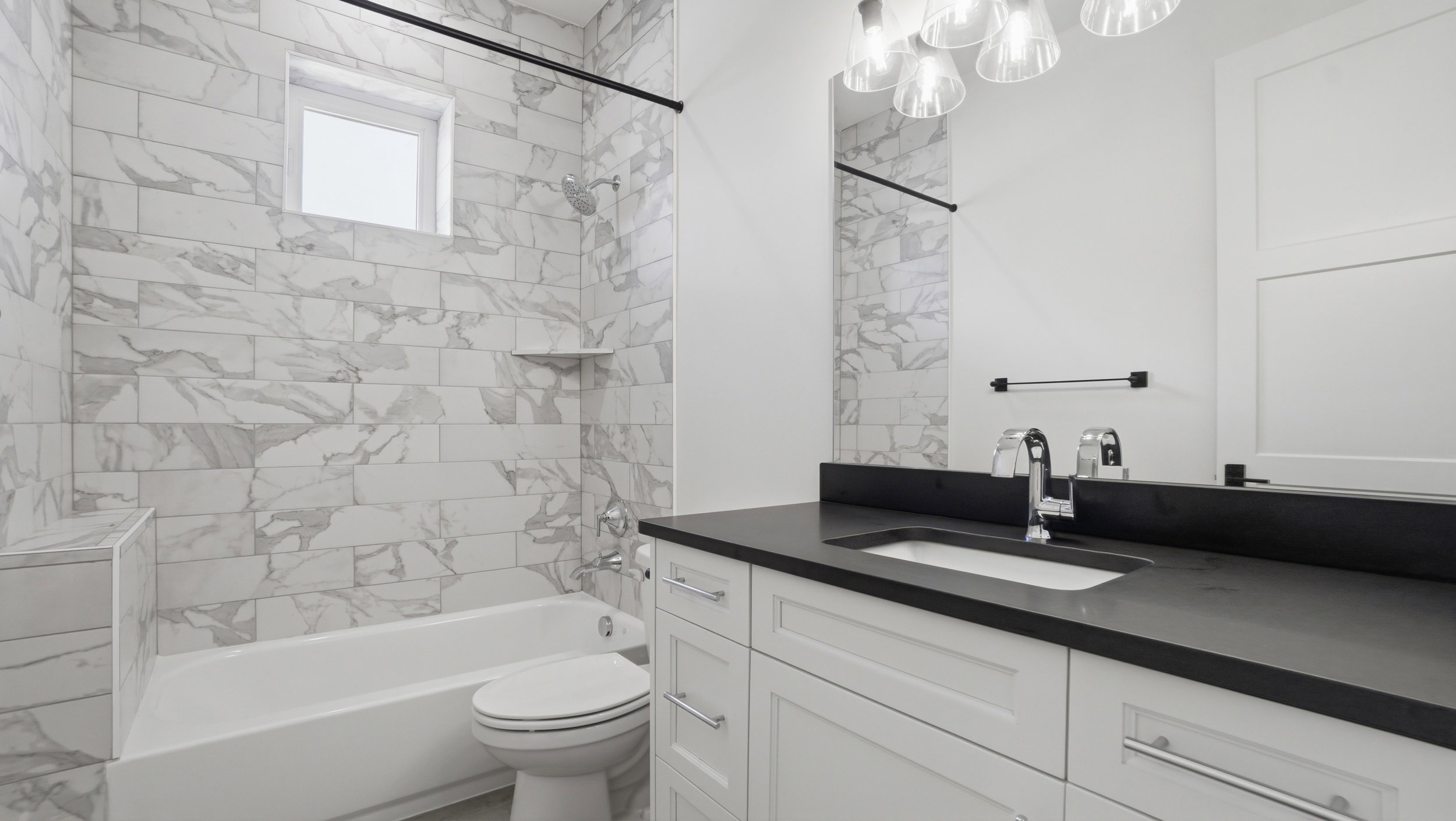 Bathroom featuring a built-in tub with a subway tile surround, a single vanity with a dark countertop, and a contemporary light fixture