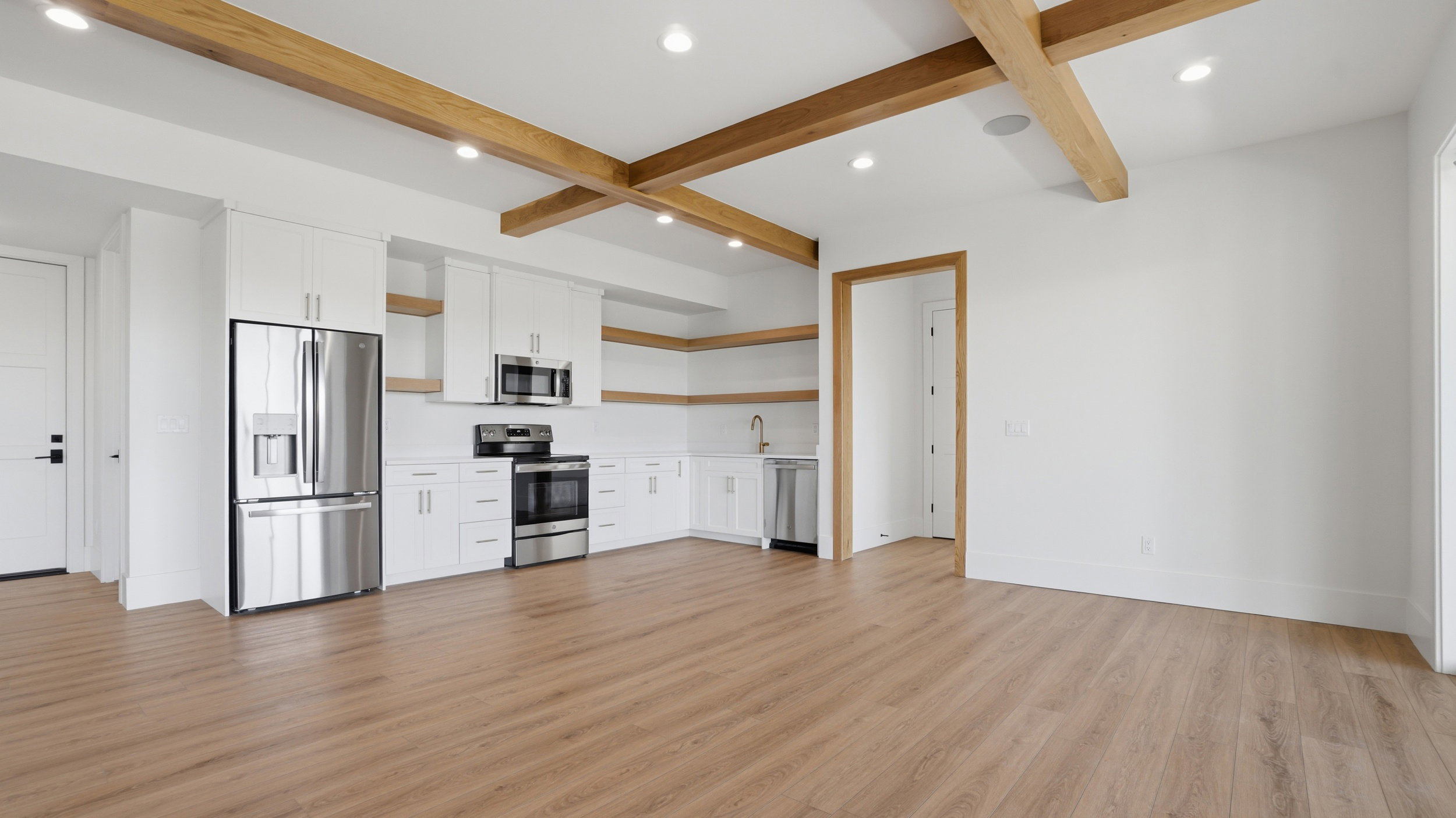 Open-concept living area featuring a full kitchen with stainless steel appliances, white cabinetry, and wood-finish flooring