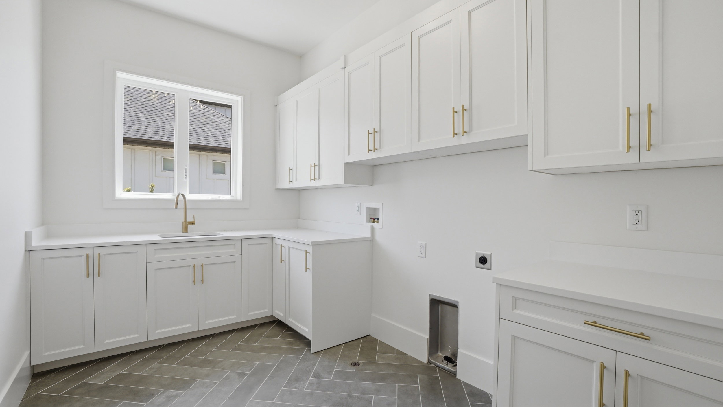 Laundry room featuring white shaker-style cabinetry with gold-tone hardware, white countertops, an undermount sink with a gooseneck faucet, and herringbone pattern floor tiles