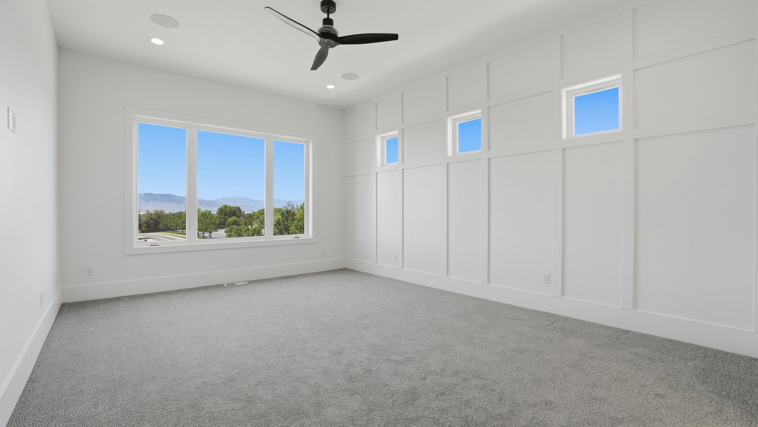 Spacious room featuring a multi-pane window with mountain scenery, board and batten accent wall with high transom windows, recessed lighting, and a ceiling fan