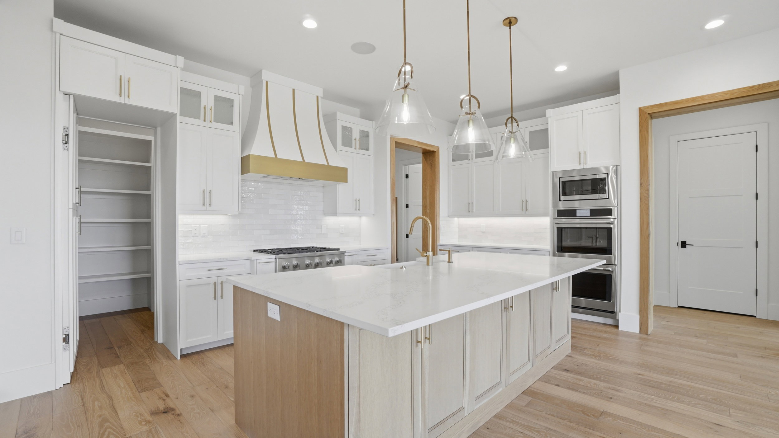 Gourmet kitchen featuring a large central island with seating, white cabinetry, integrated stainless steel appliances, a walk-in pantry, and wood-finish flooring