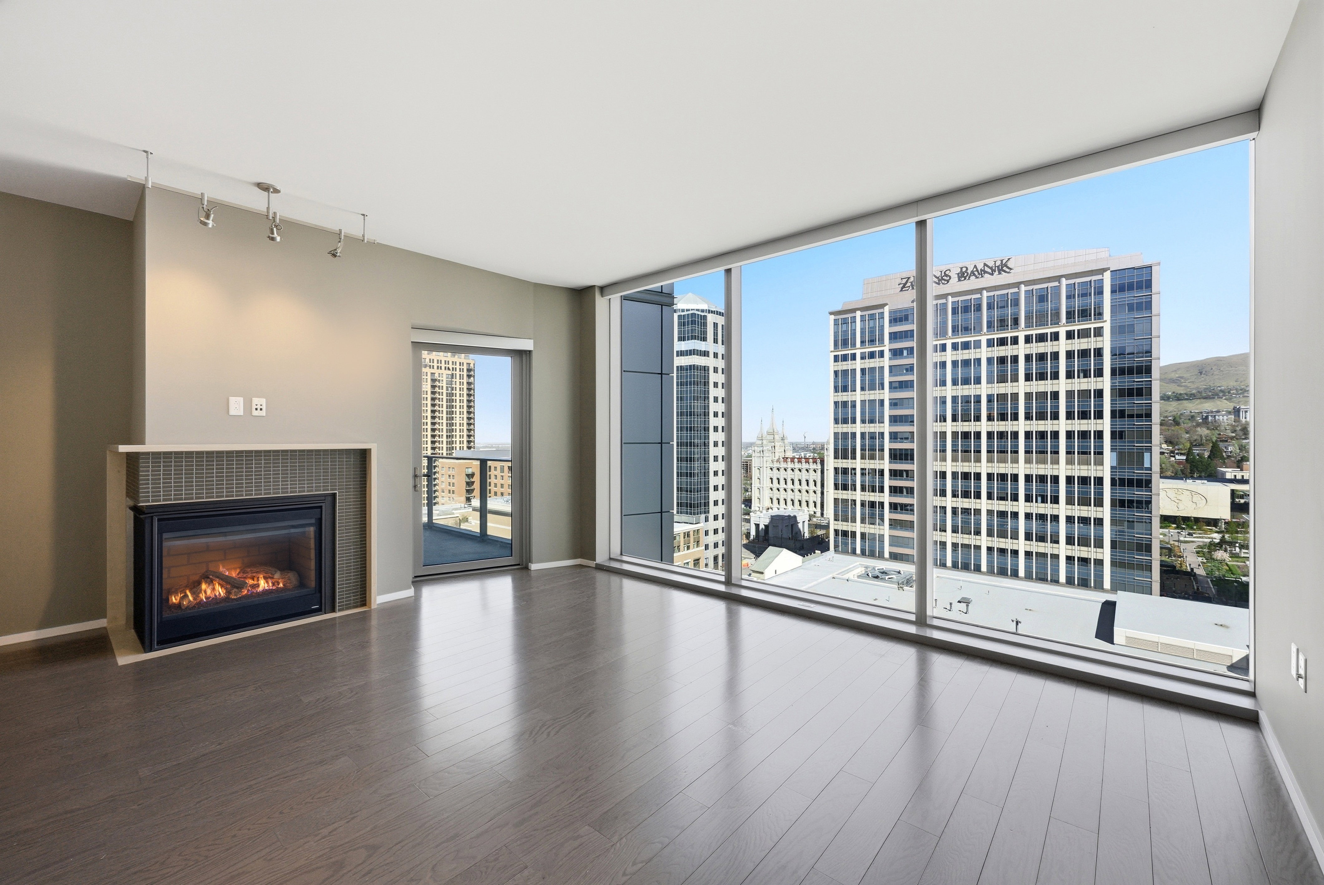 Expansive room featuring dark wood-finish flooring, a contemporary fireplace with a tiled surround and hearth, track lighting, and a glass-paneled door leading to an outdoor space