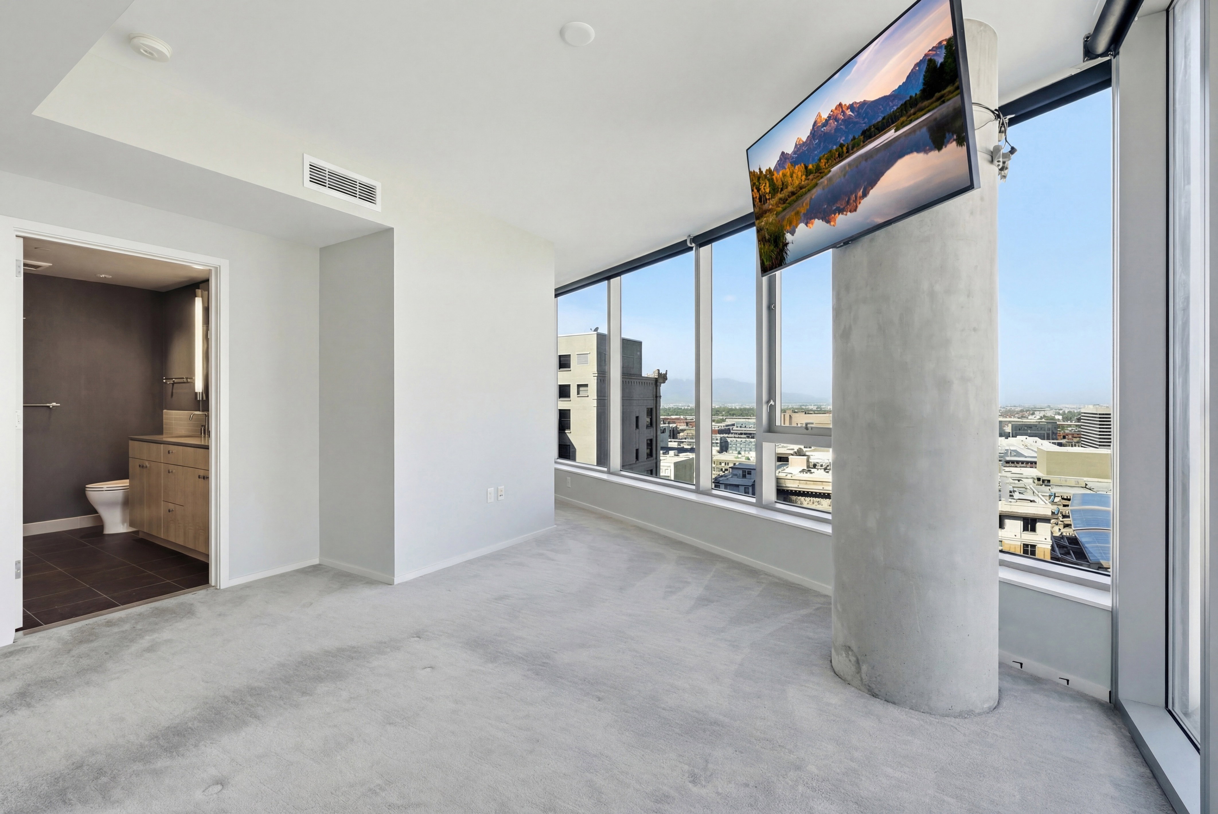 Light gray carpeted room featuring a concrete pillar and expansive window walls offering urban scenery