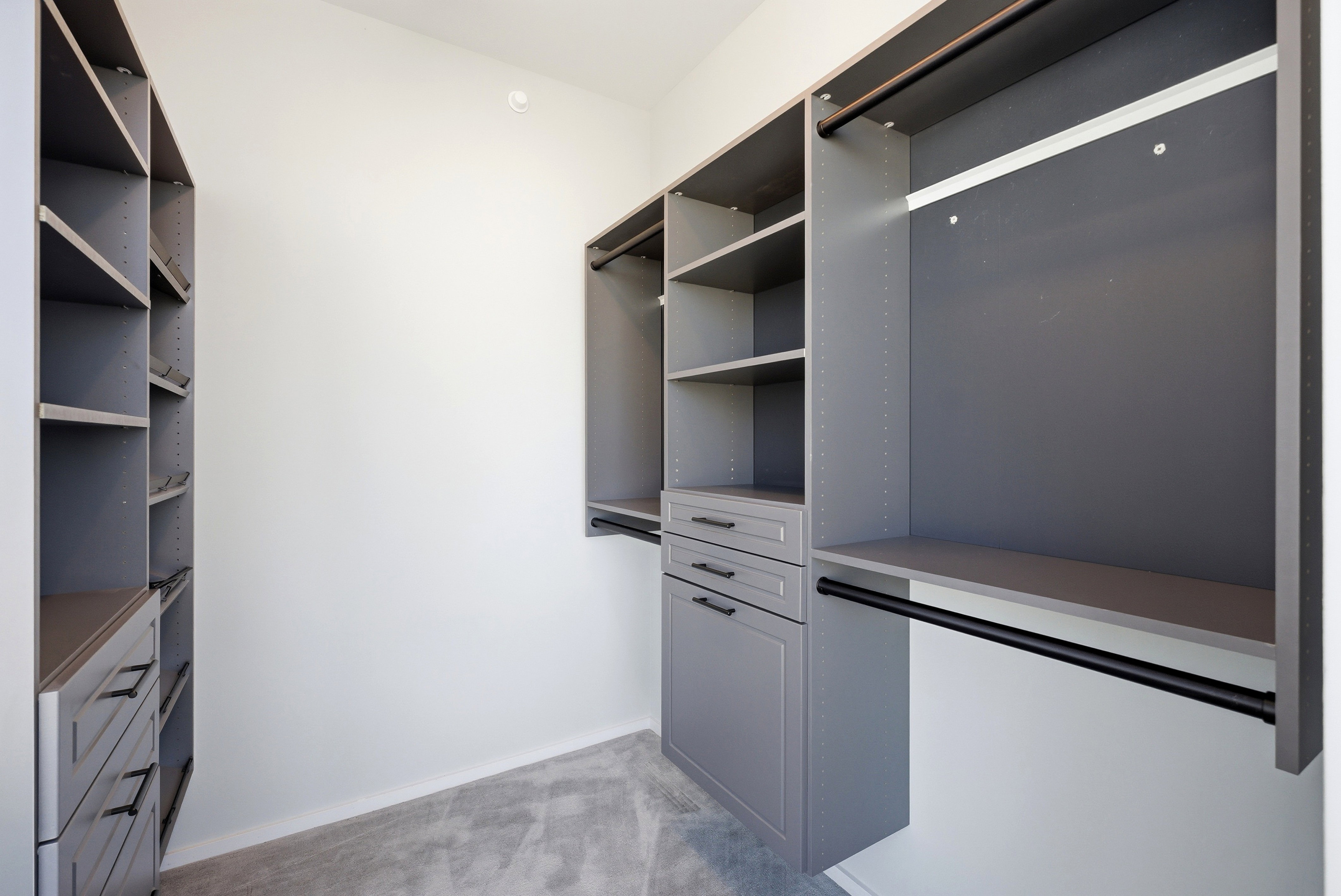 Custom storage system featuring gray cabinetry, integrated shelving, three drawers with dark hardware, and multiple hanging rods