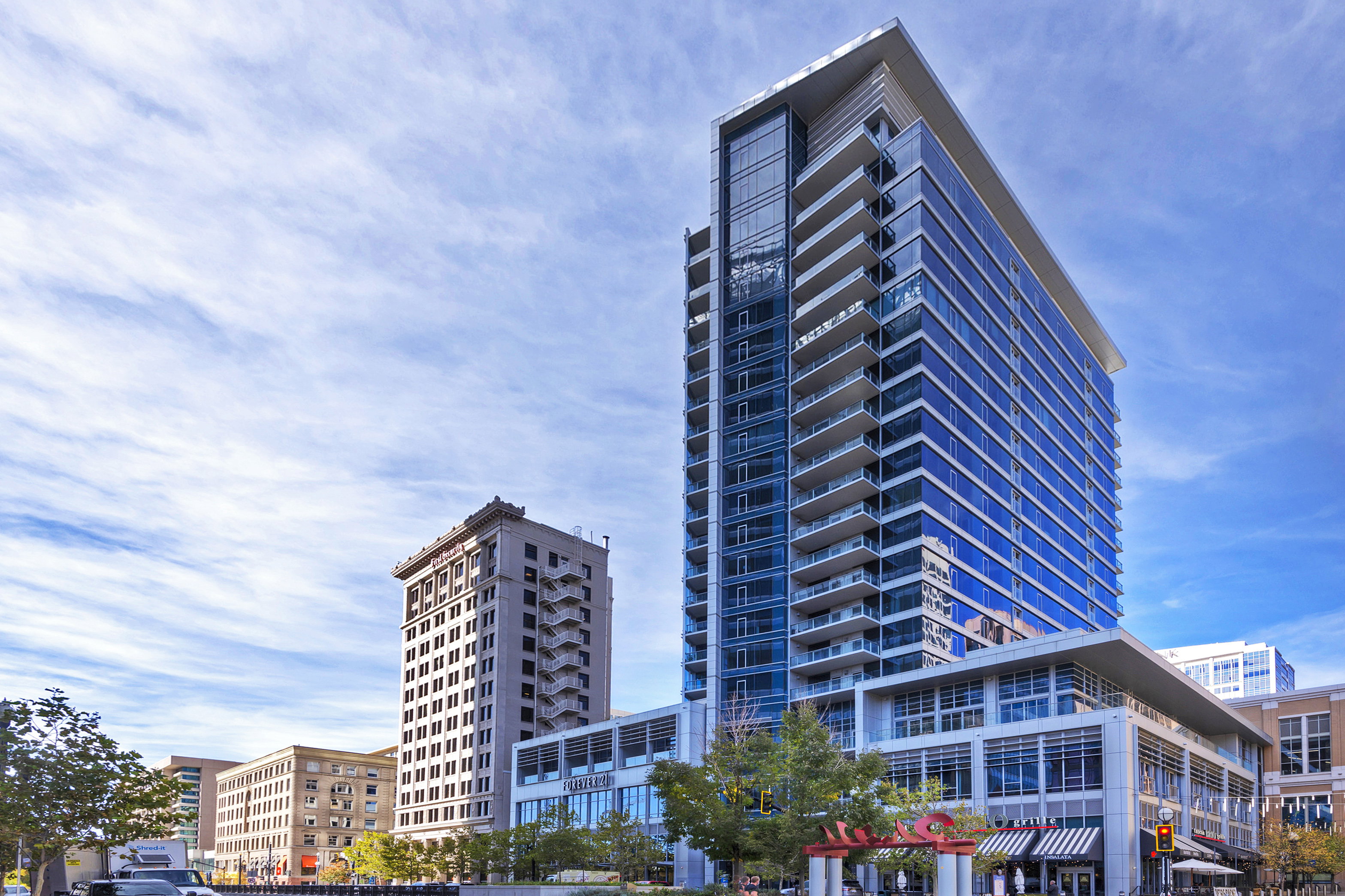 Modern high-rise building featuring extensive glass curtain walls, multiple private balconies, and a distinctive rooftop overhang
