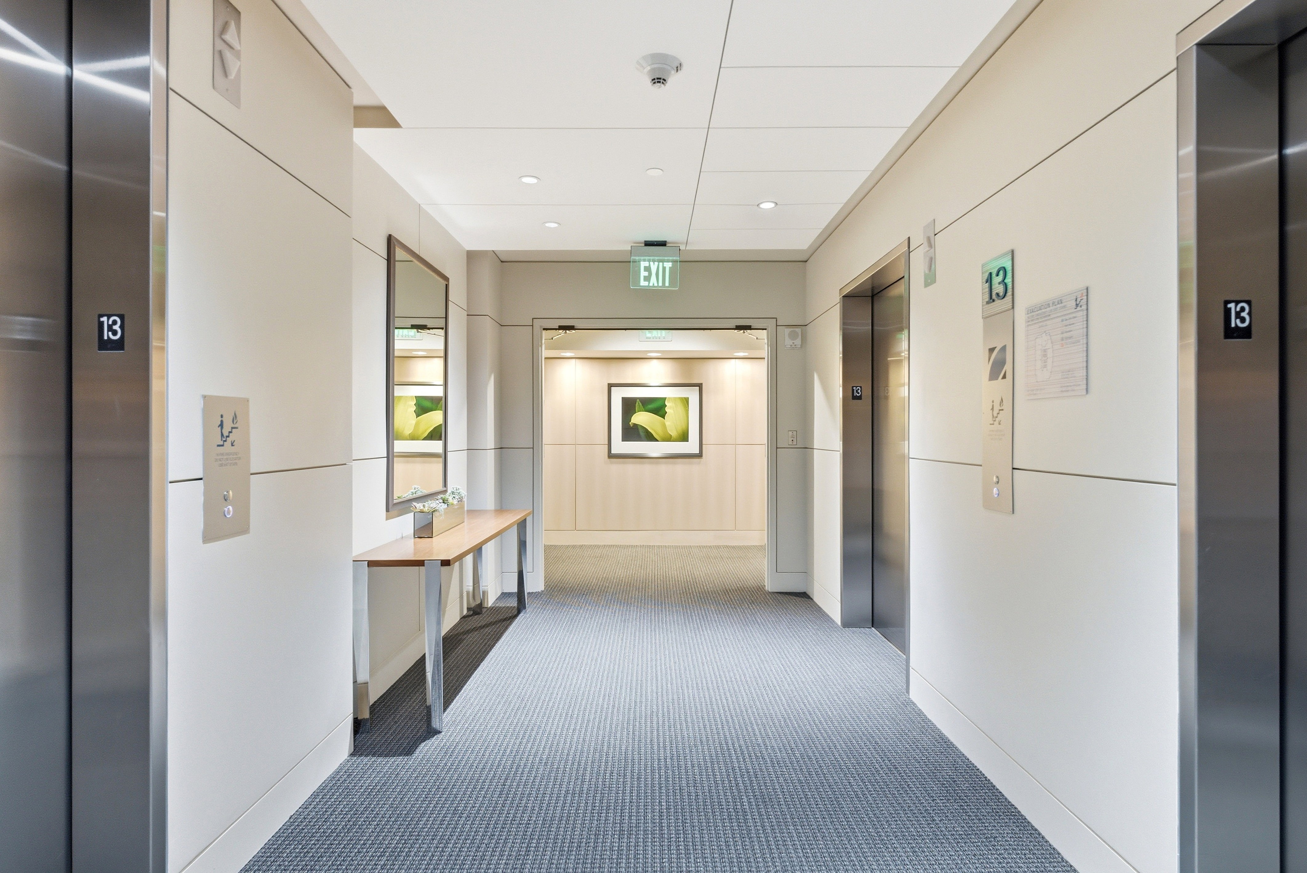 Hallway featuring two stainless steel elevators, recessed lighting, carpet flooring, and a console table with a mirror