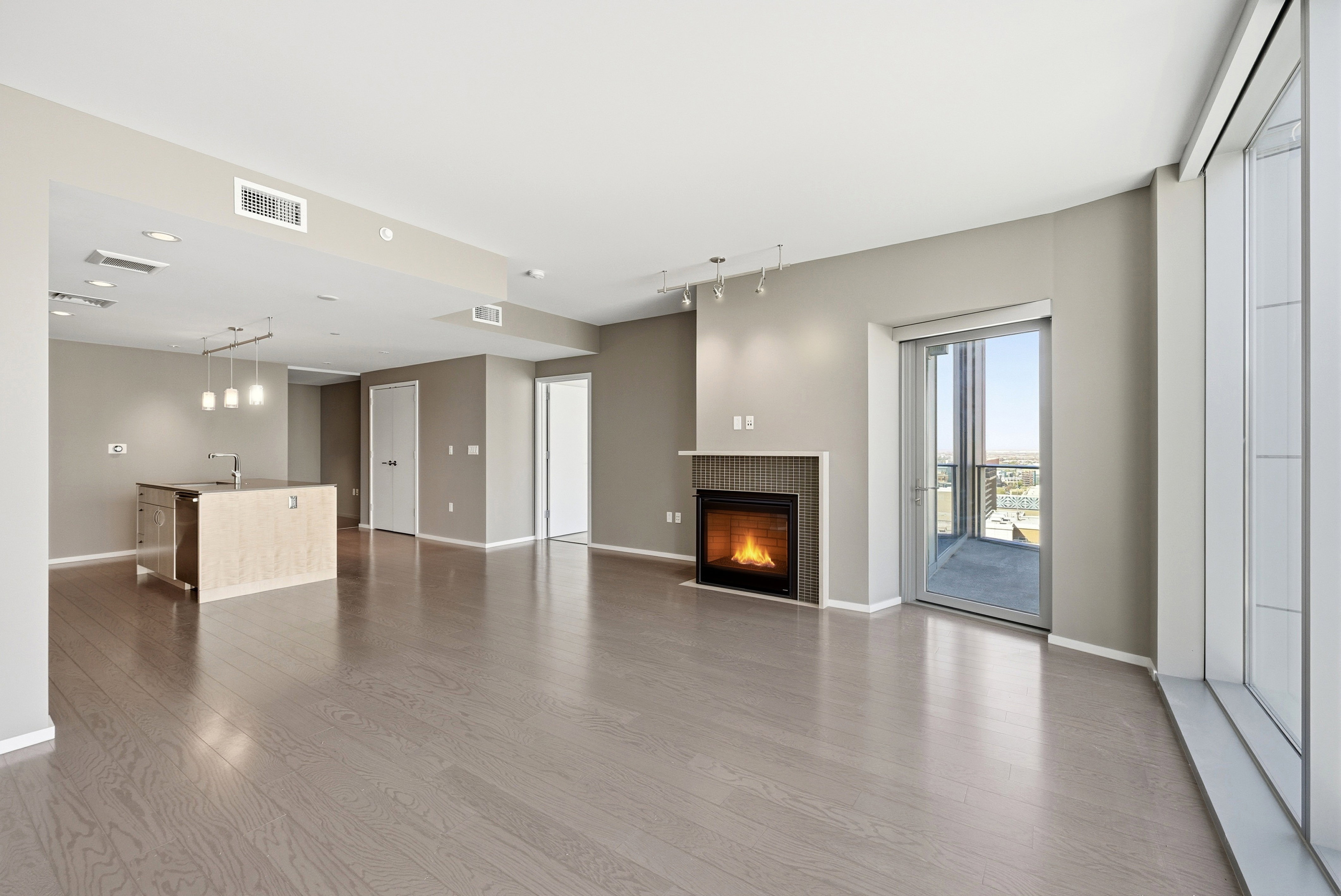 Open-concept living area featuring wood-finish flooring, a contemporary fireplace with a fluted surround, and a kitchen island with pendant lighting