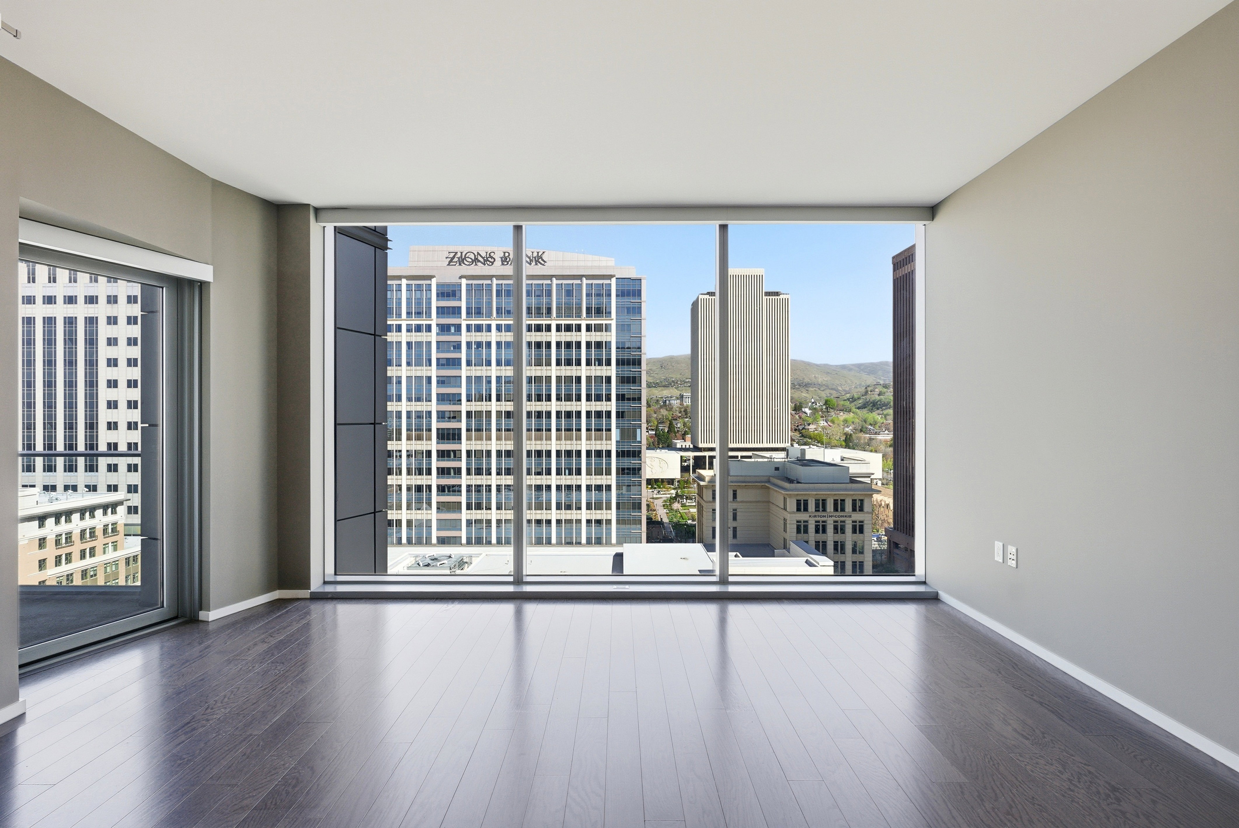 Spacious room featuring floor-to-ceiling windows, dark wood-finish flooring, and a sliding glass door opening to a balcony