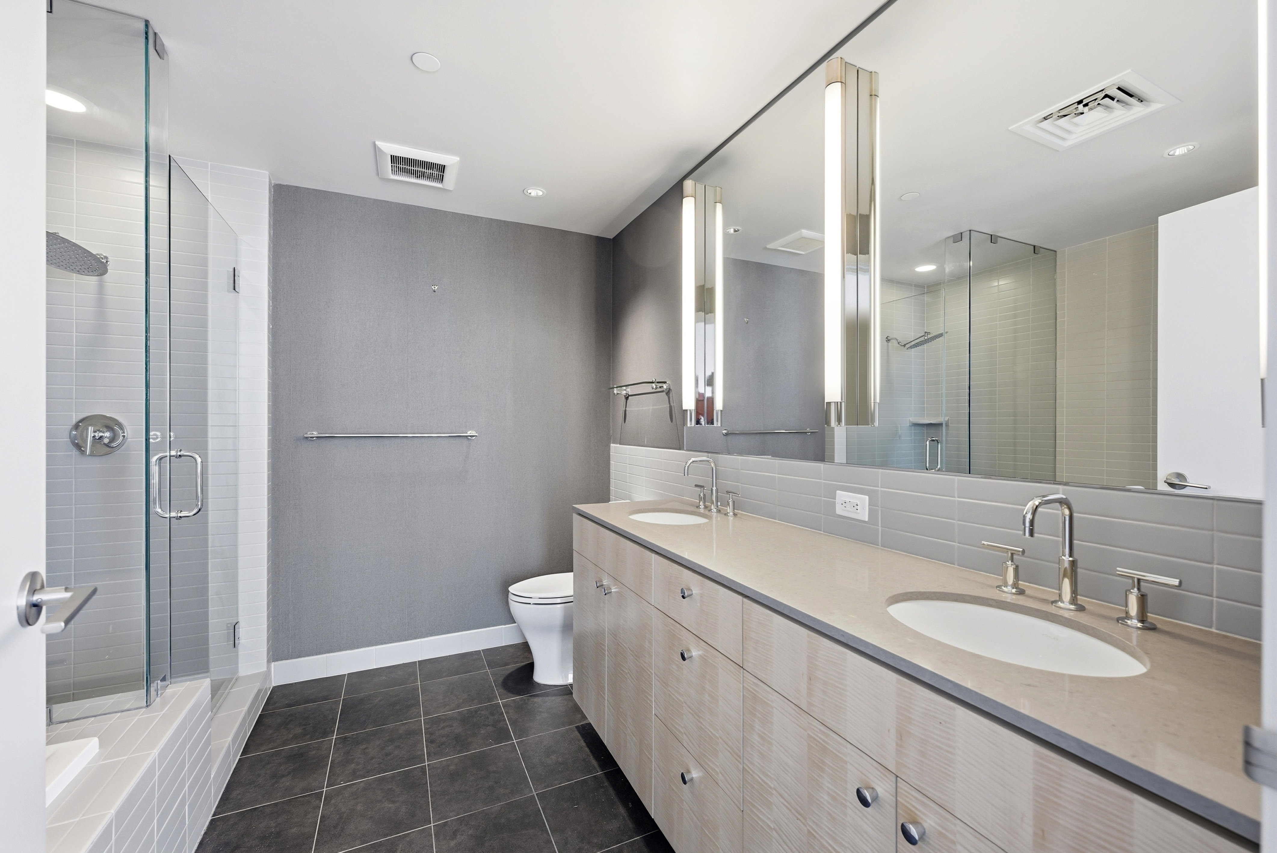 Bathroom featuring a glass-enclosed shower, dual vanity with undermount sinks, and a full-length mirror with integrated vertical lighting