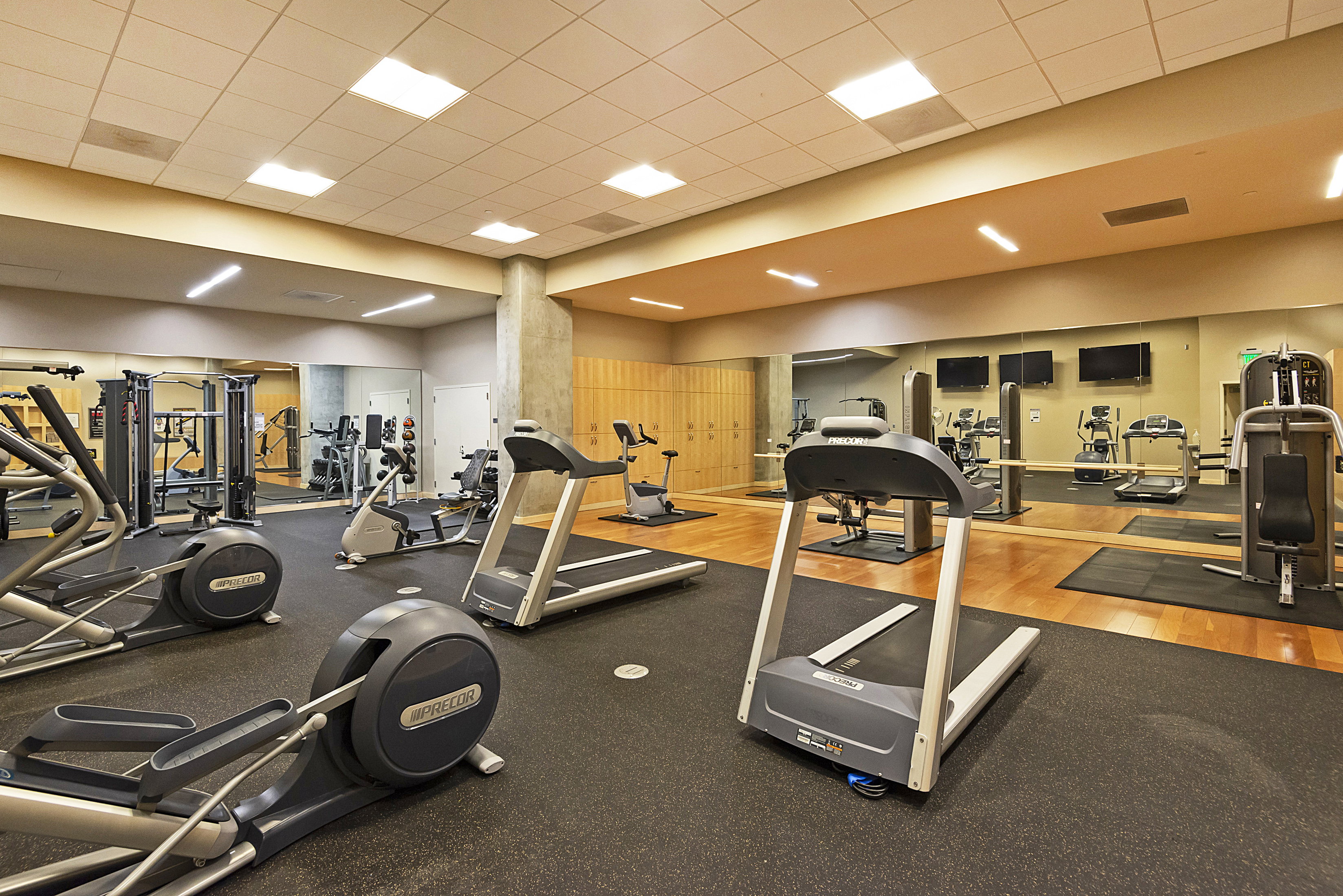 Fitness center featuring a range of cardio equipment, strength training machines, mirrored walls, wood-finish flooring, and integrated ceiling lighting