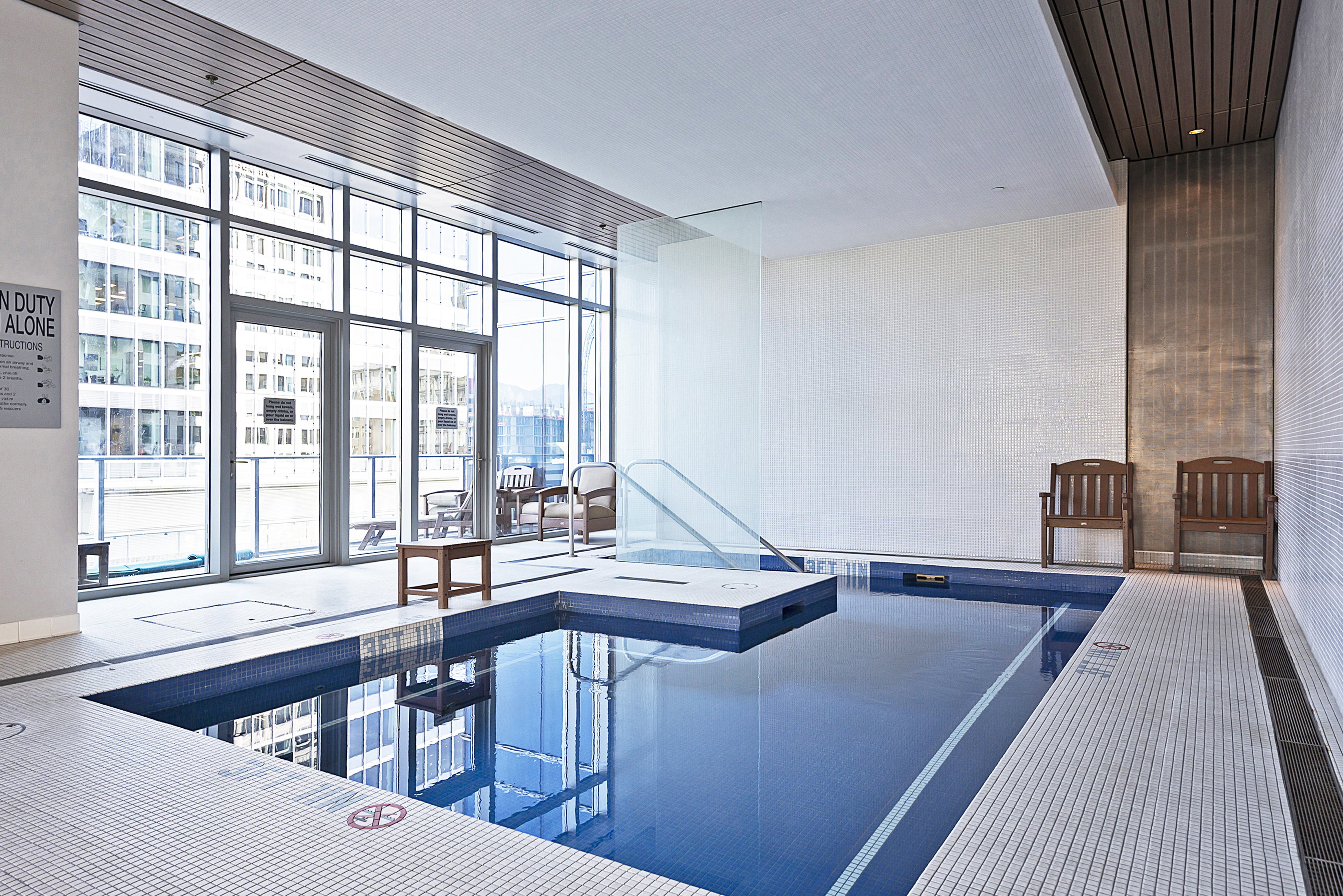 Indoor swimming pool featuring blue mosaic tiling and a white tiled surround
