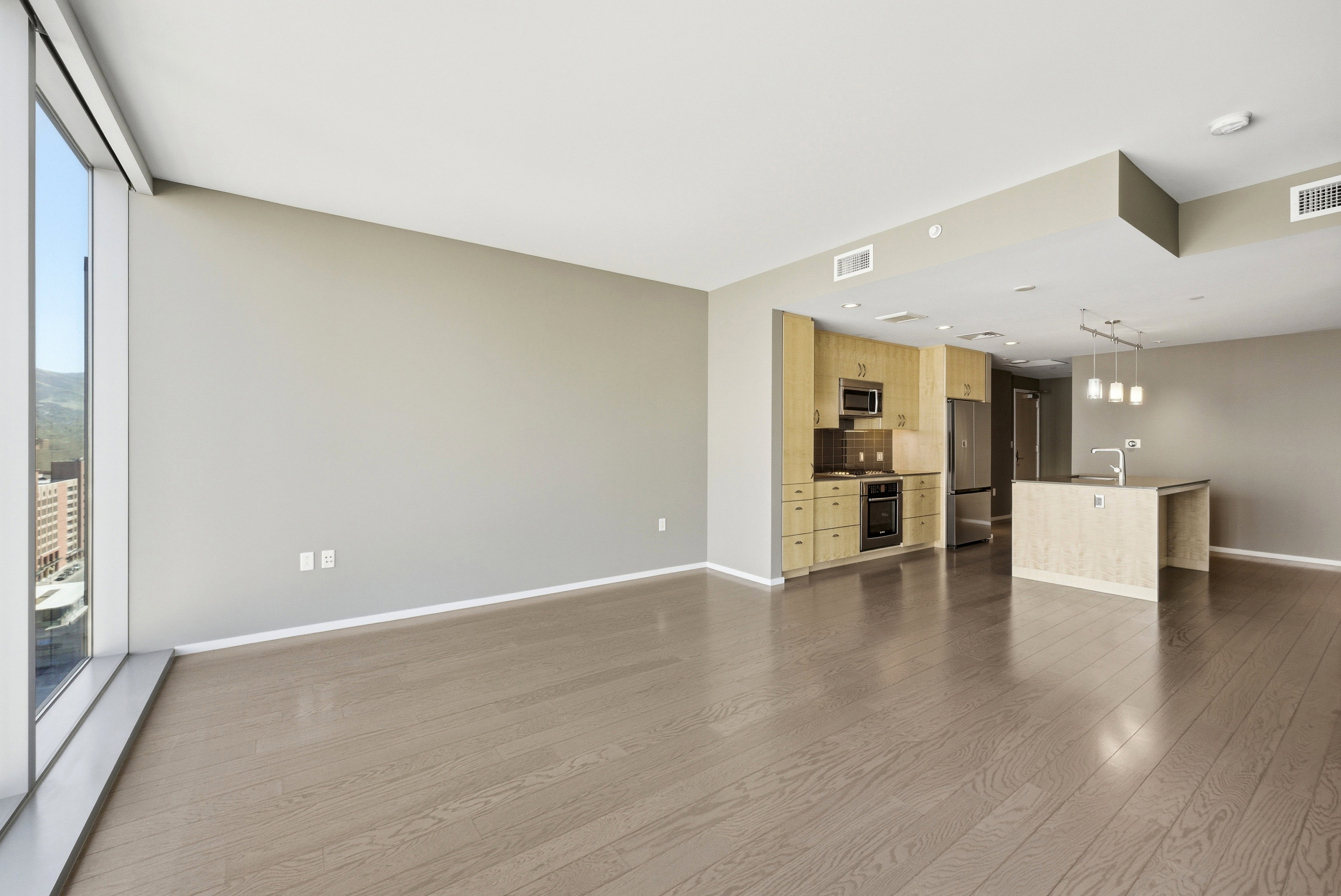 Open-concept living space featuring wood-finish flooring, a full-height window, a kitchen island with a sink, a built-in oven, and a stainless steel refrigerator