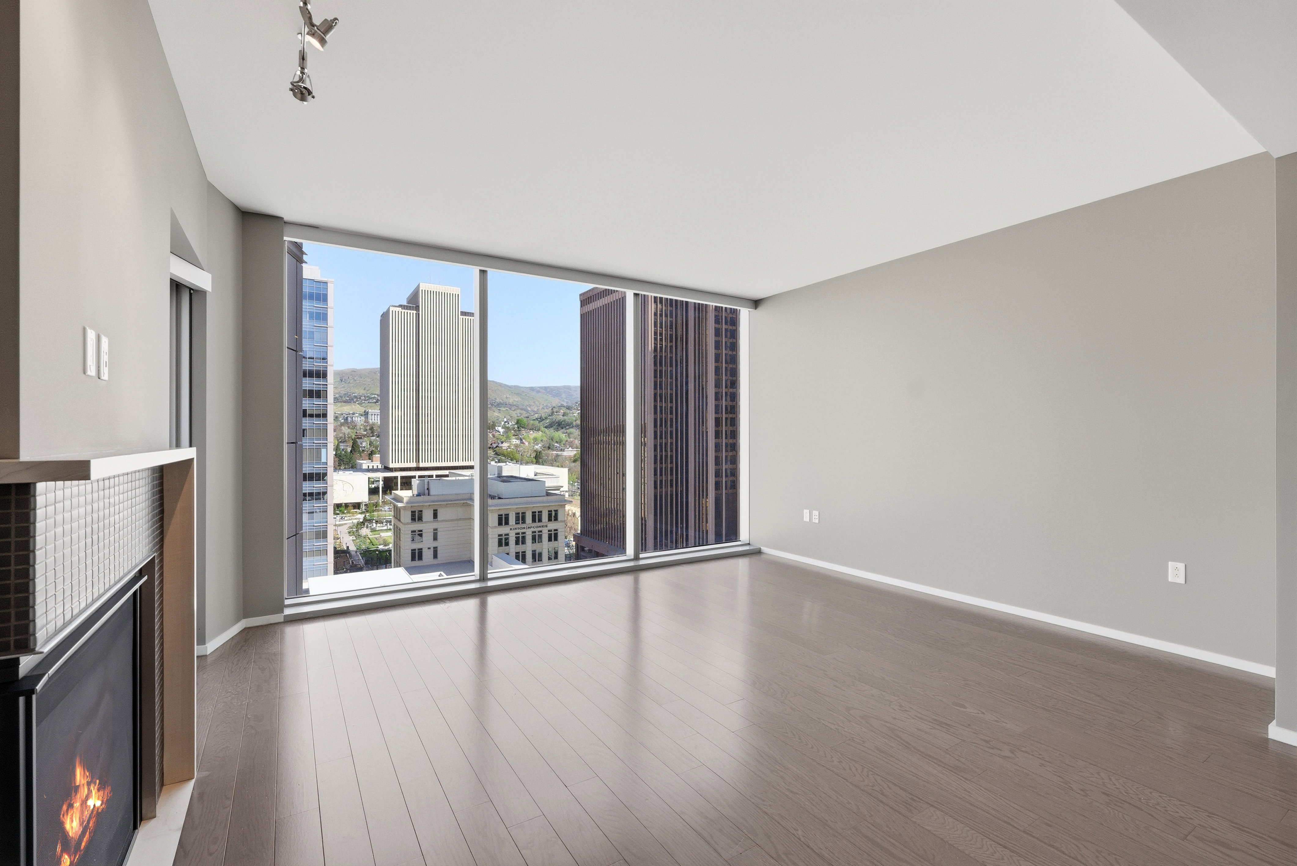 Expansive living area featuring a fireplace with a tiled surround and light-toned mantle, wood-finish flooring, recessed lighting, and floor-to-ceiling windows