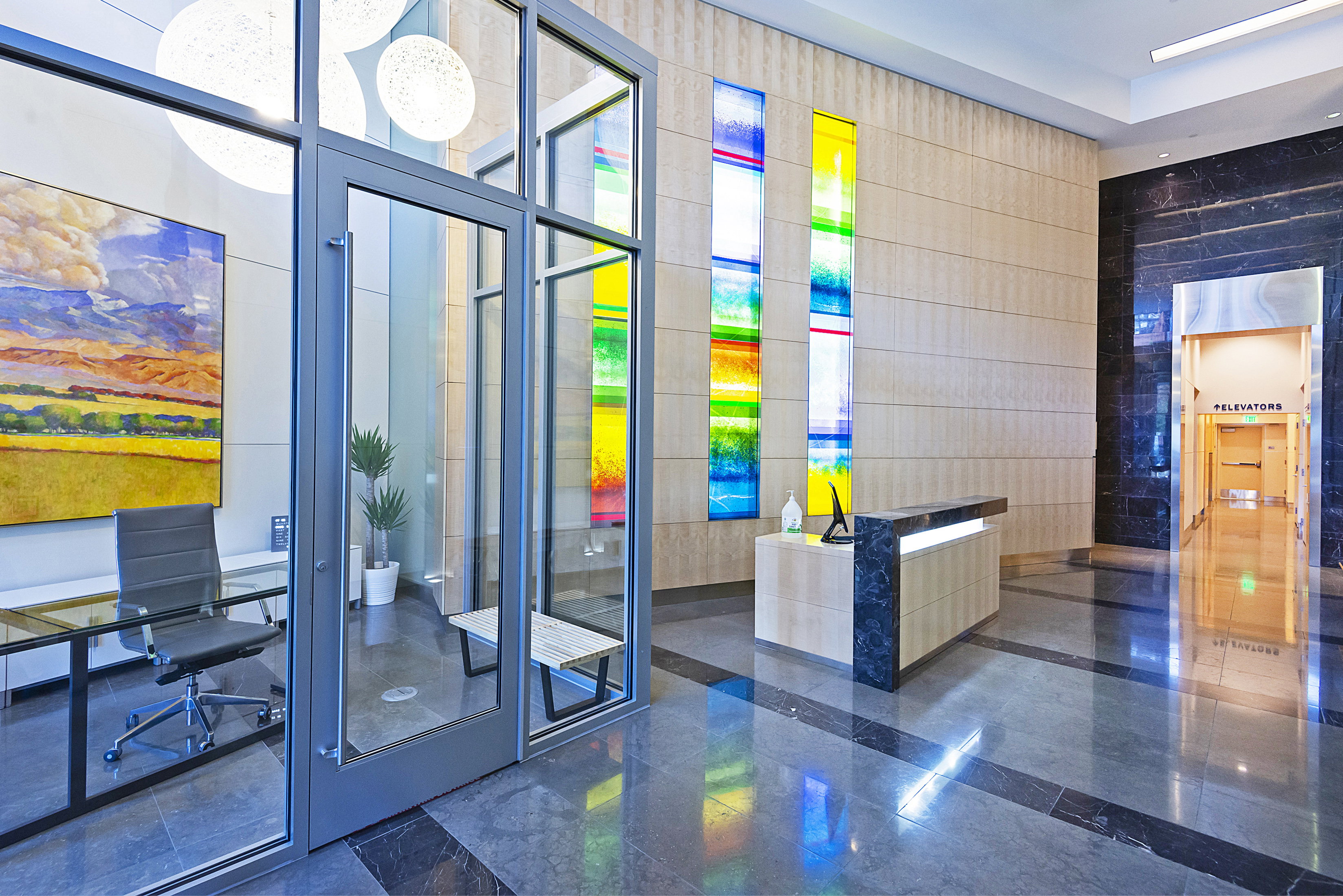 Spacious lobby featuring polished stone flooring, a contemporary reception desk, decorative stained glass wall panels, and an enclosed office space with glass walls