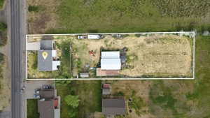 Expansive property featuring a residence with a gray shingle roof, a detached auxiliary building with a white metal roof, and a large undeveloped lot