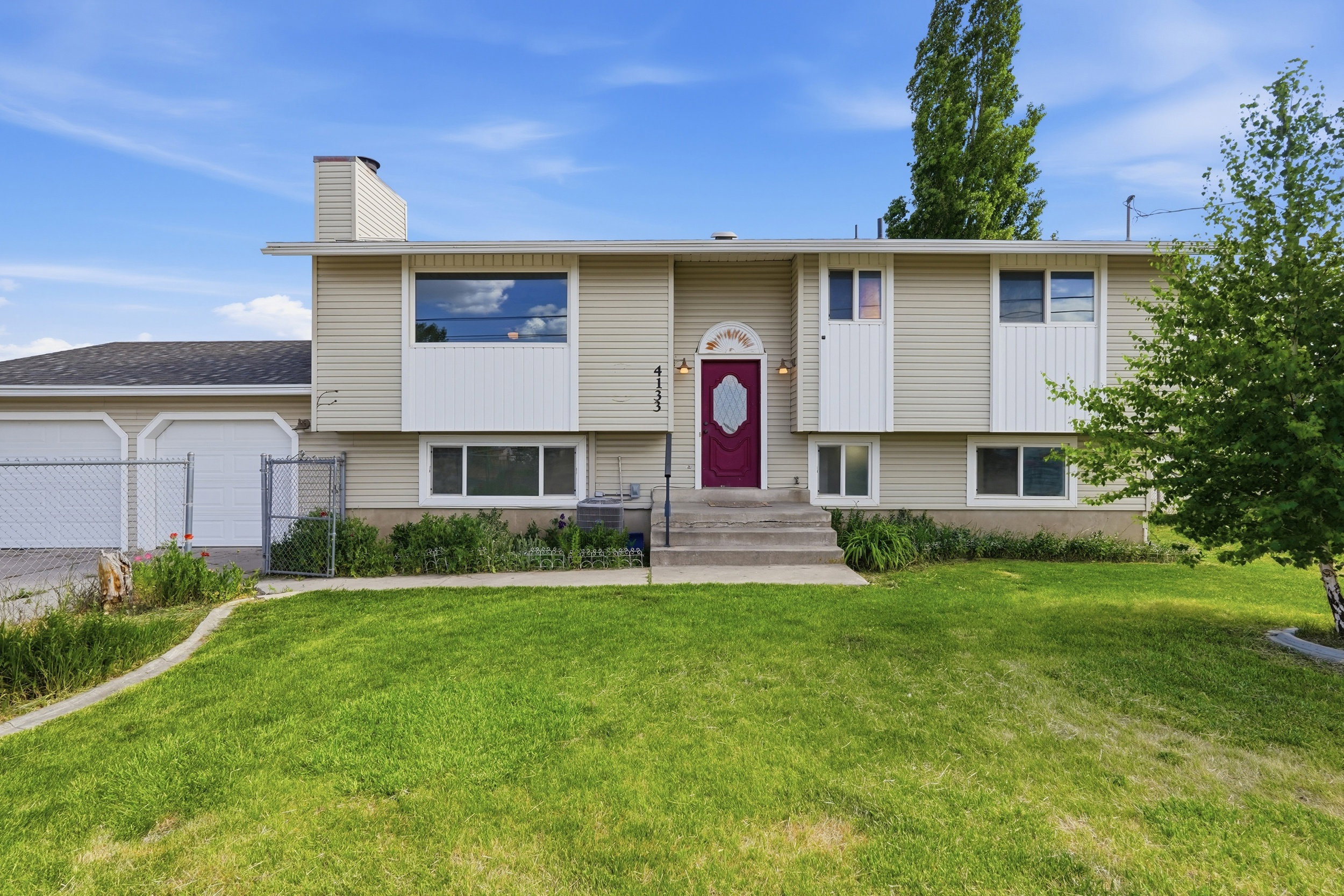 Split-level residence featuring light-colored siding and a contrasting red entry door with decorative glass