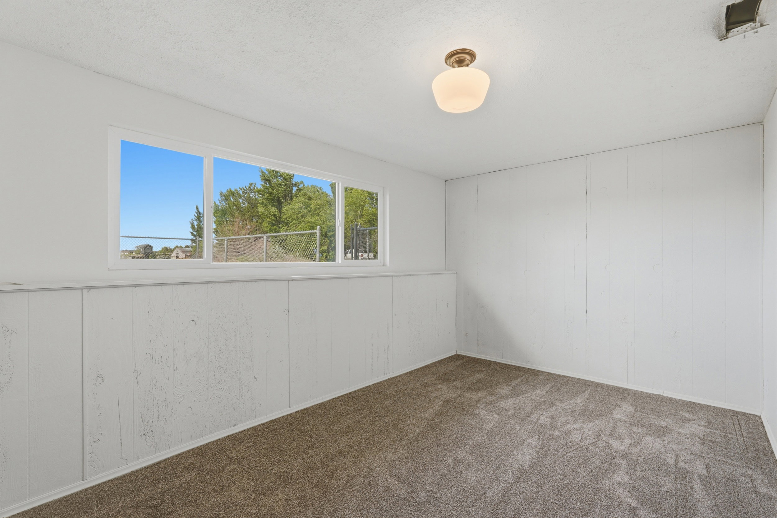Bright room featuring a large horizontal window, white paneled walls, and neutral-toned carpet flooring