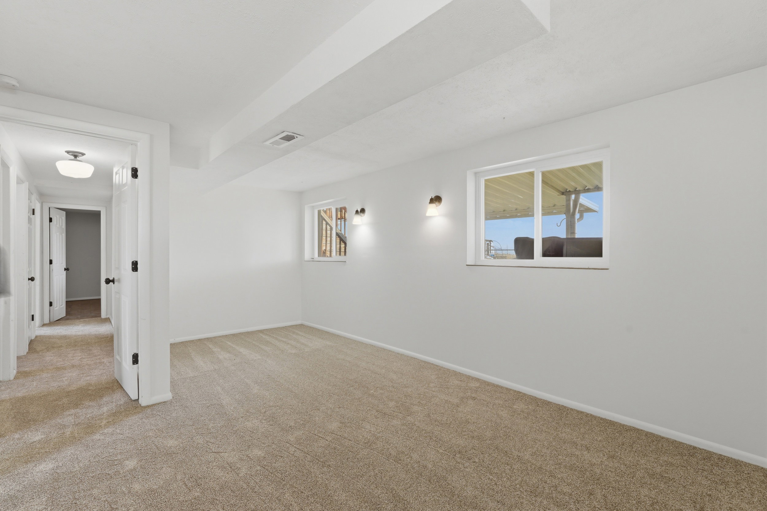 Carpeted room featuring white walls, two wall-mounted sconces, and a white-framed window