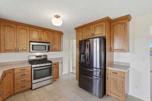 Kitchen featuring extensive wood cabinetry, stainless steel oven/range, built-in microwave, dark stainless steel refrigerator, and tiled flooring